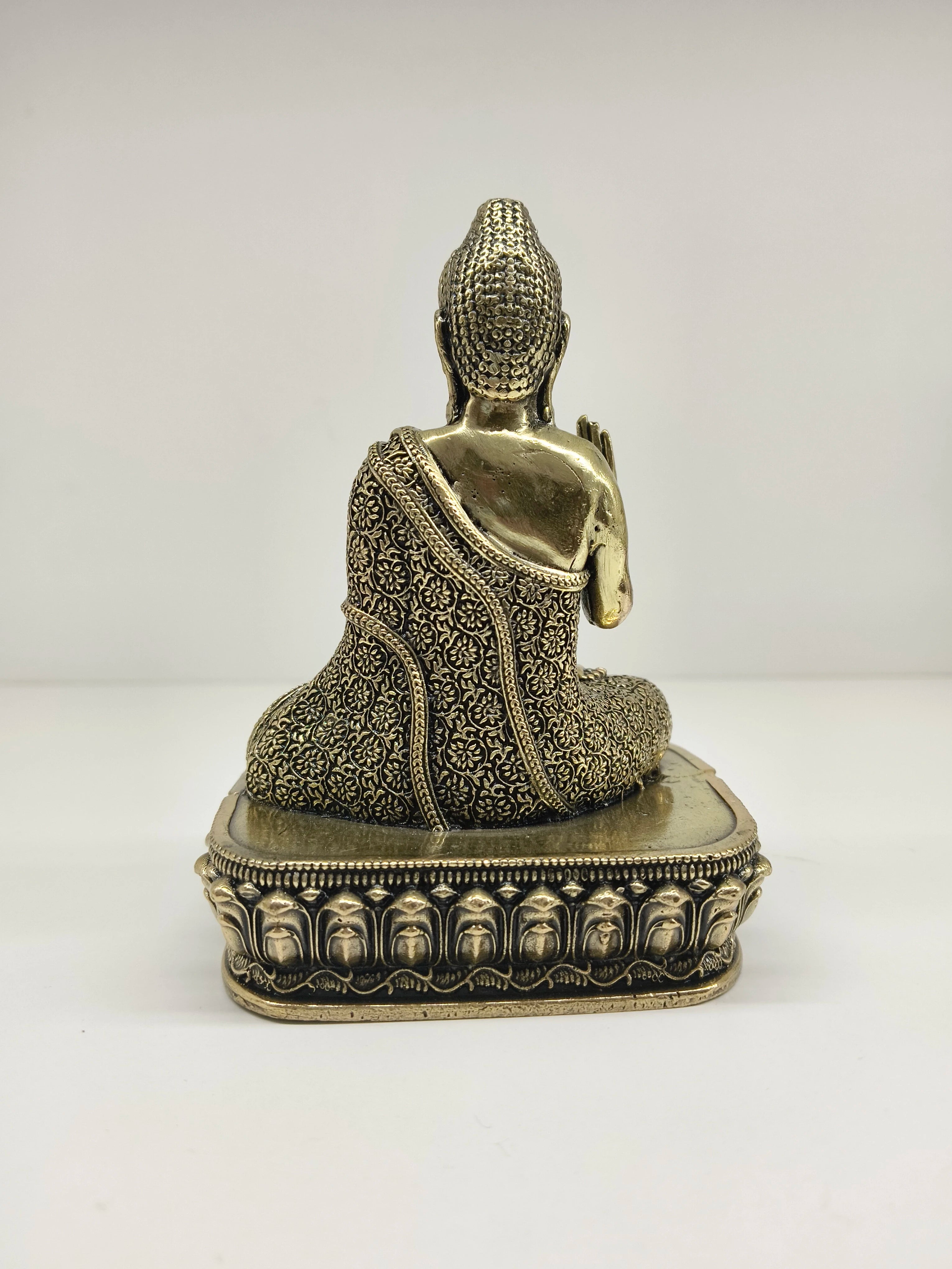 Back view of small brass Buddha statue with intricate patterned robe on ornate base