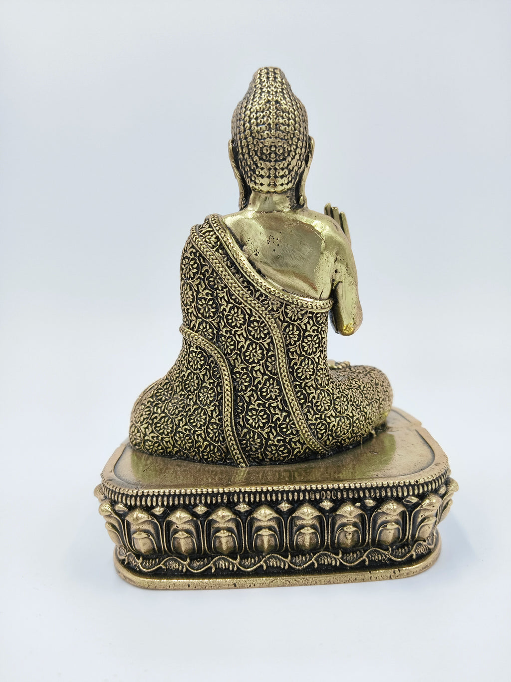 Back view of small brass Buddha statue with intricate patterned robe on ornate base