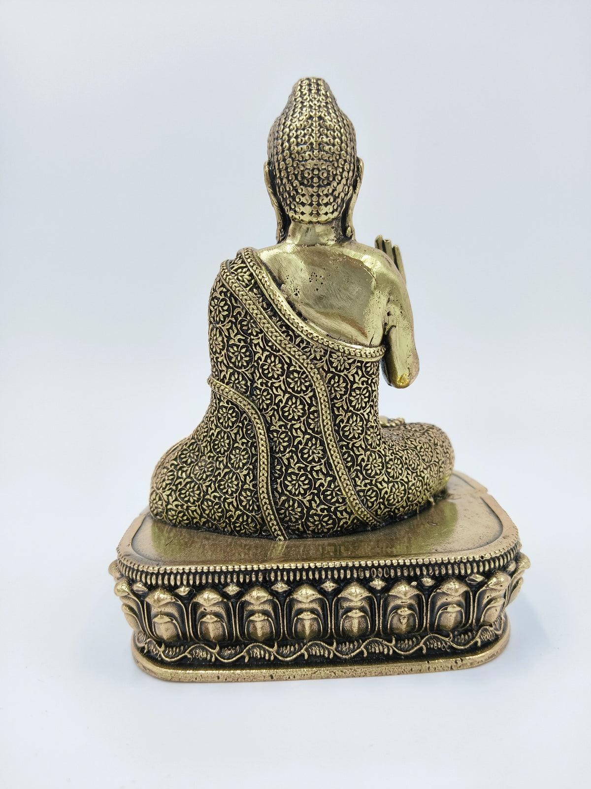 Back view of small brass Buddha statue with intricate patterned robe on ornate base