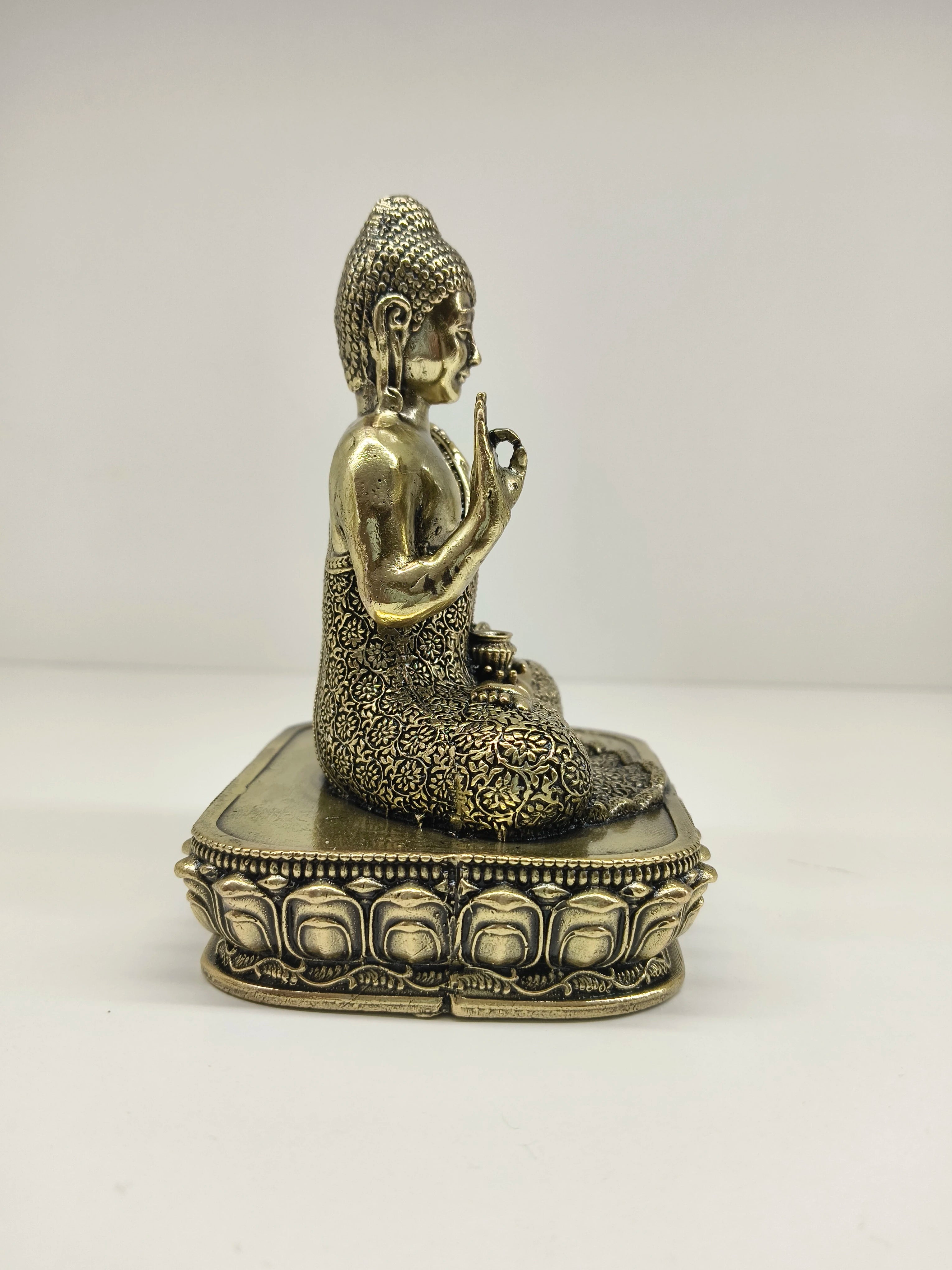 Side view of small brass Buddha statue seated on ornate pedestal