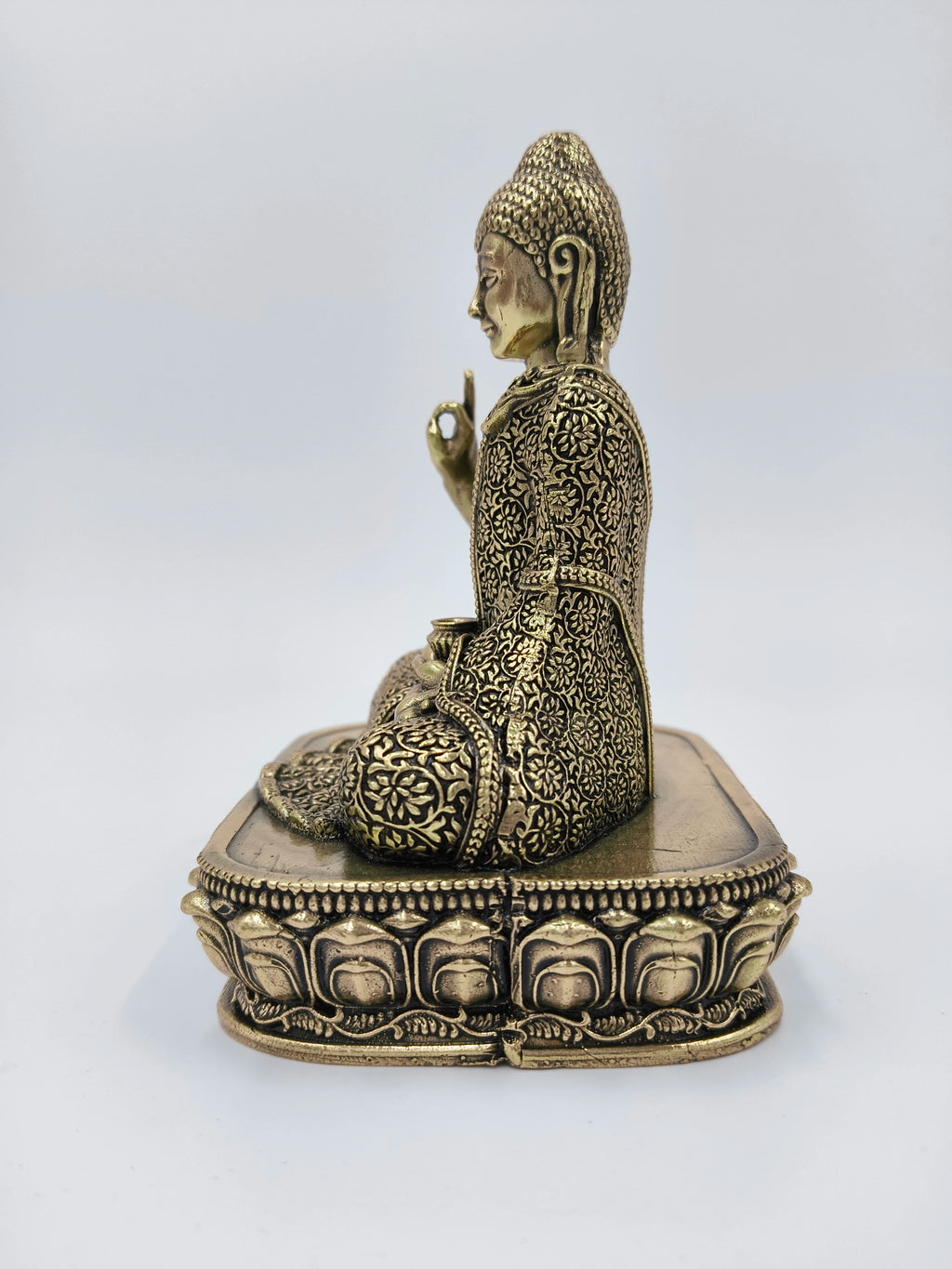 Side view of small brass Buddha statue seated on ornate pedestal