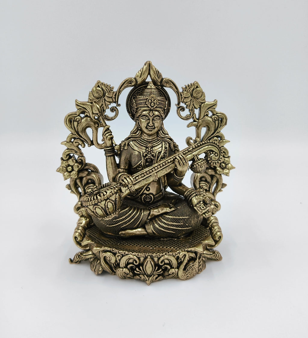Small brass Saraswathi idol seated with veena and decorative floral backdrop