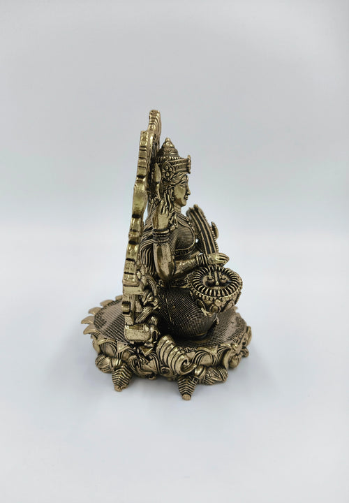 Side view of small brass Saraswathi sculpture seated on ornamental base