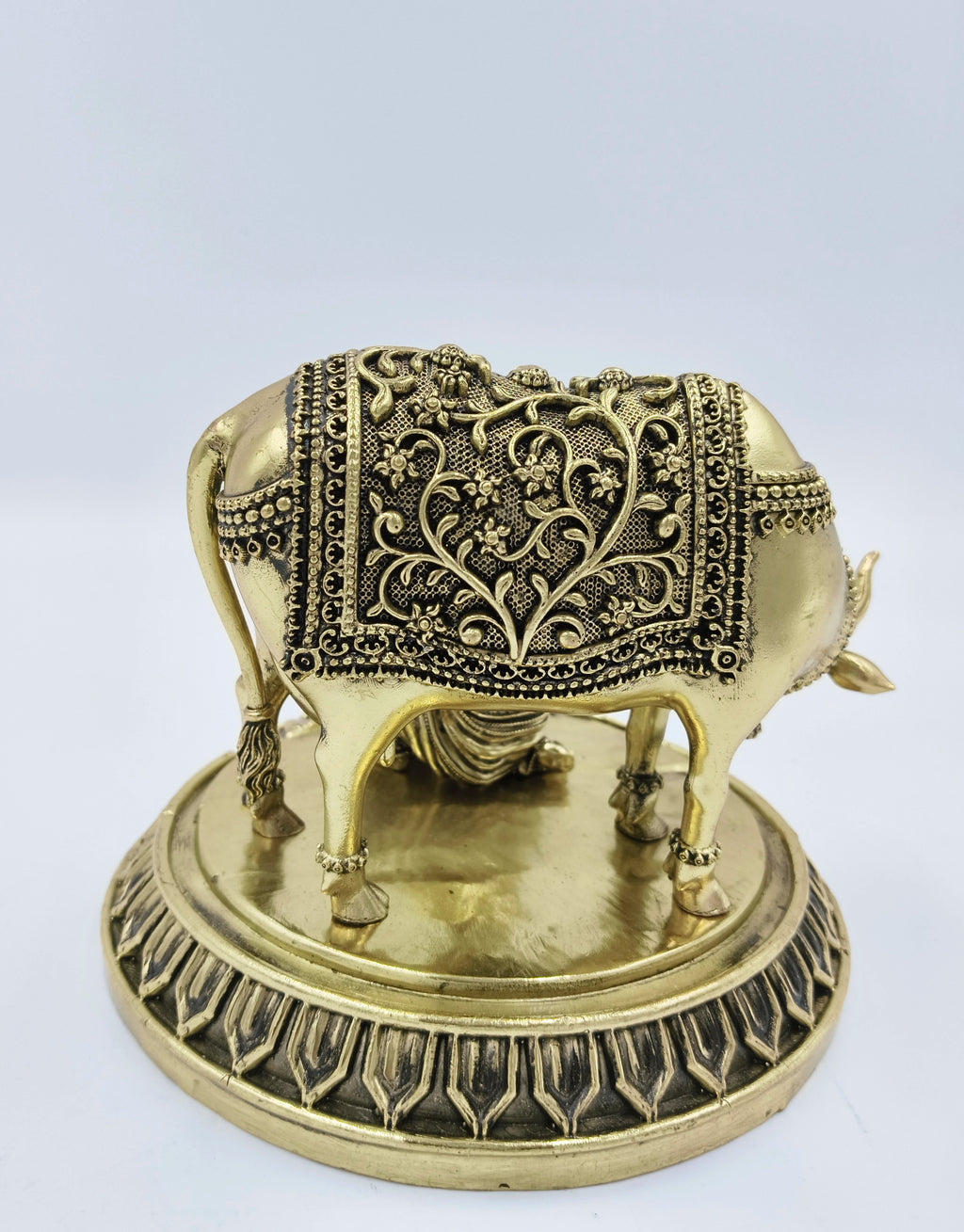 Brass sculpted cow with floral patterned covering on decorative base, side view