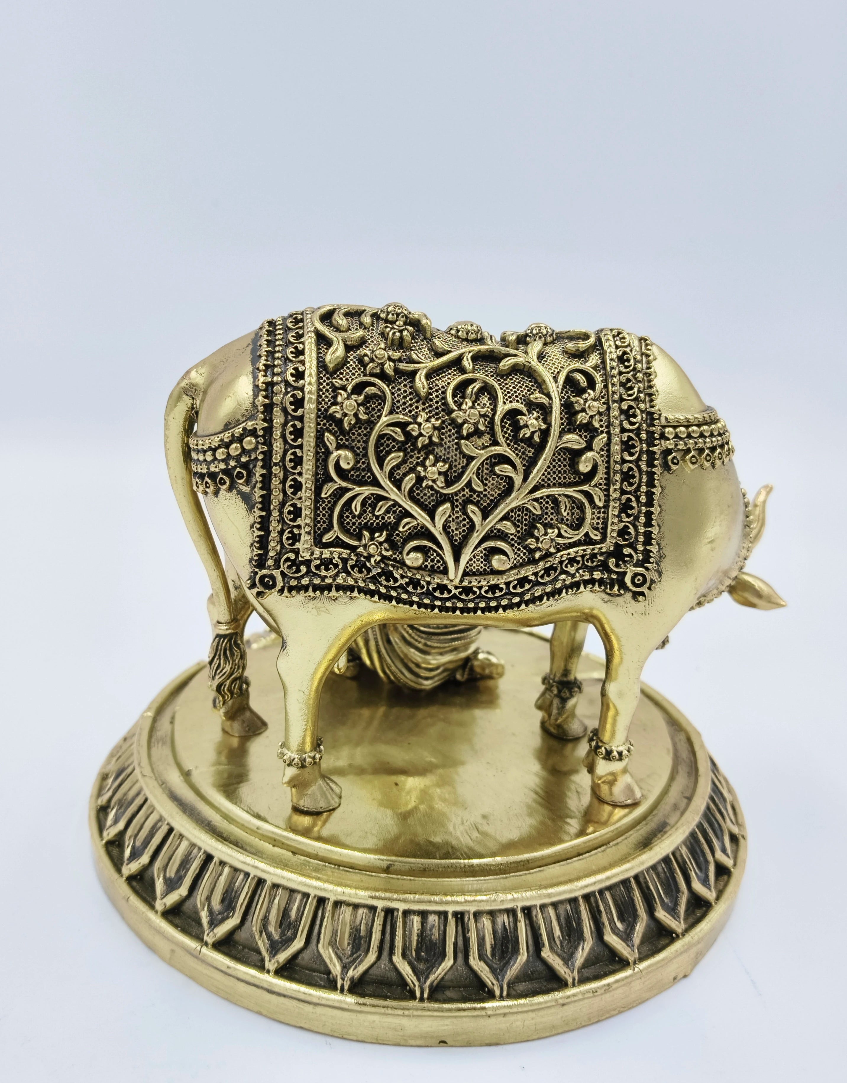 Brass sculpted cow with floral patterned covering on decorative base, side view