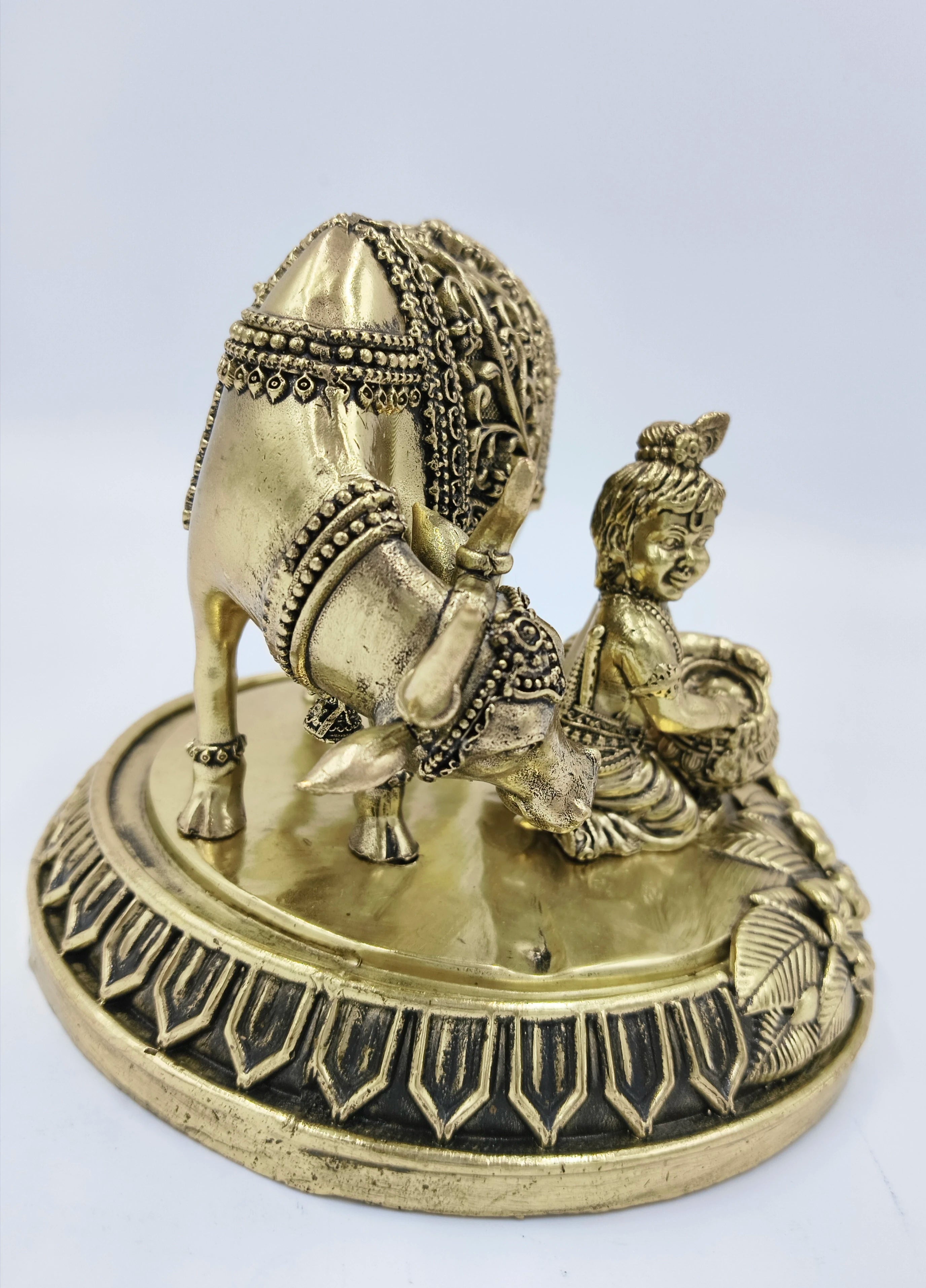 Brass sculpture of Krishna playing with a decorated cow on round base, side view