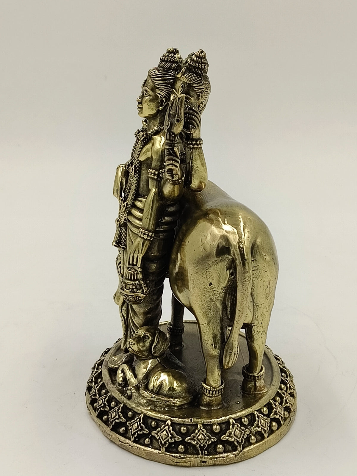 Side view of brass Dattatreya statue with cow and dog on decorative base