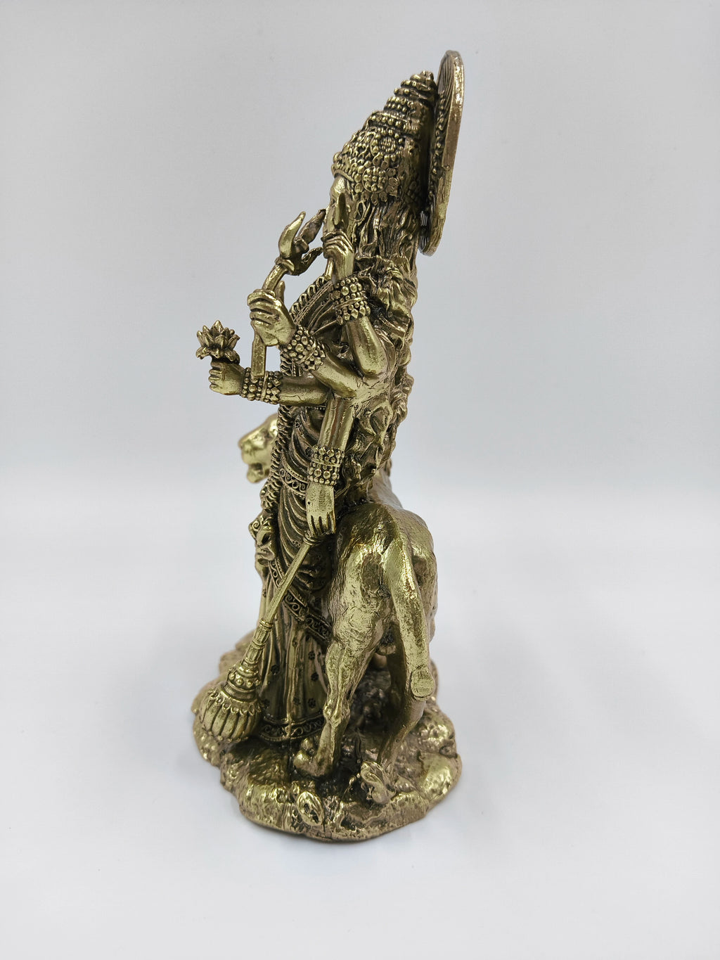 Side view of a medium brass Durgeshwari statue with multiple arms holding weapons