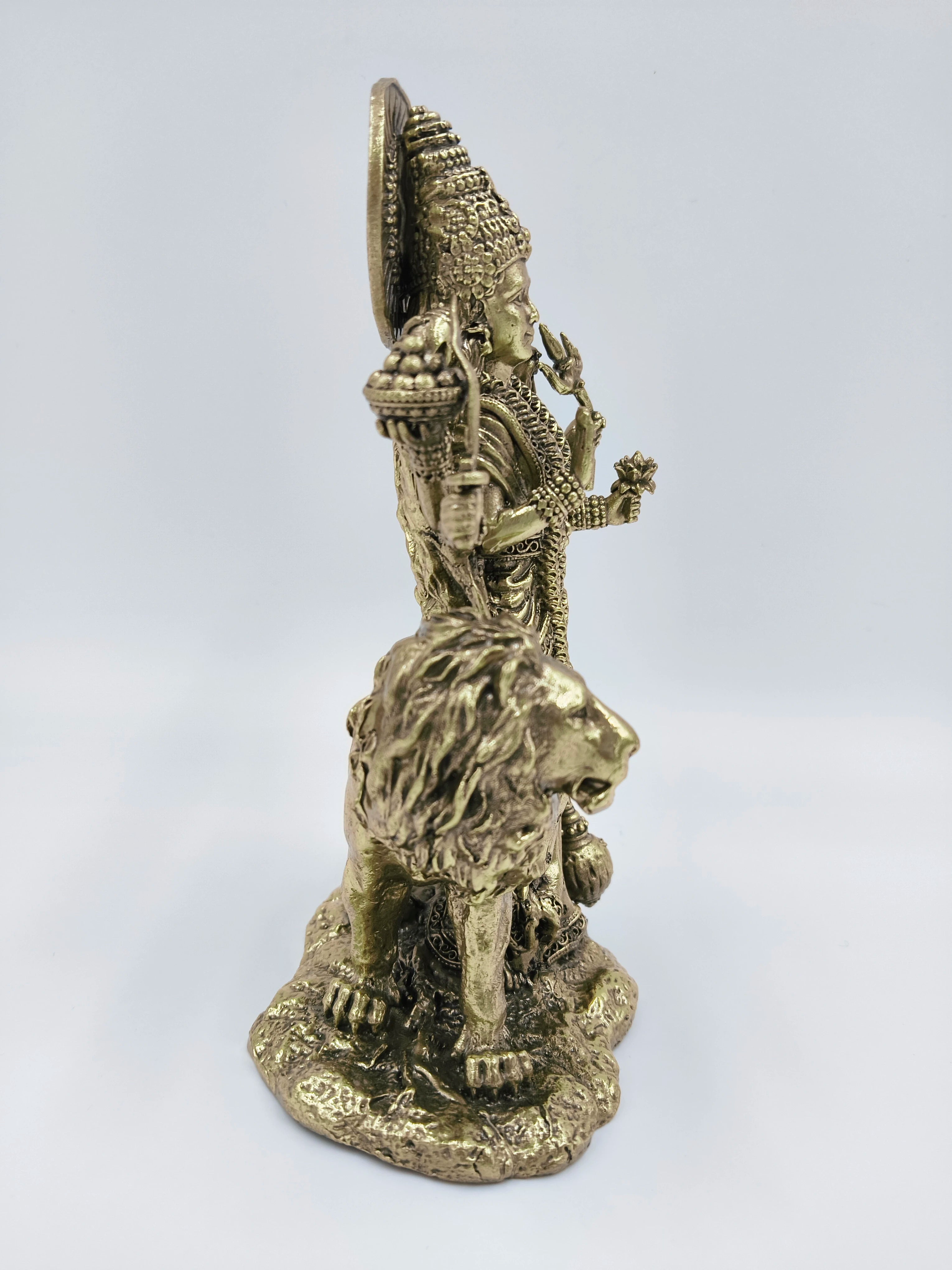 Side view of a brass Durgeshwari statue standing on a lion base