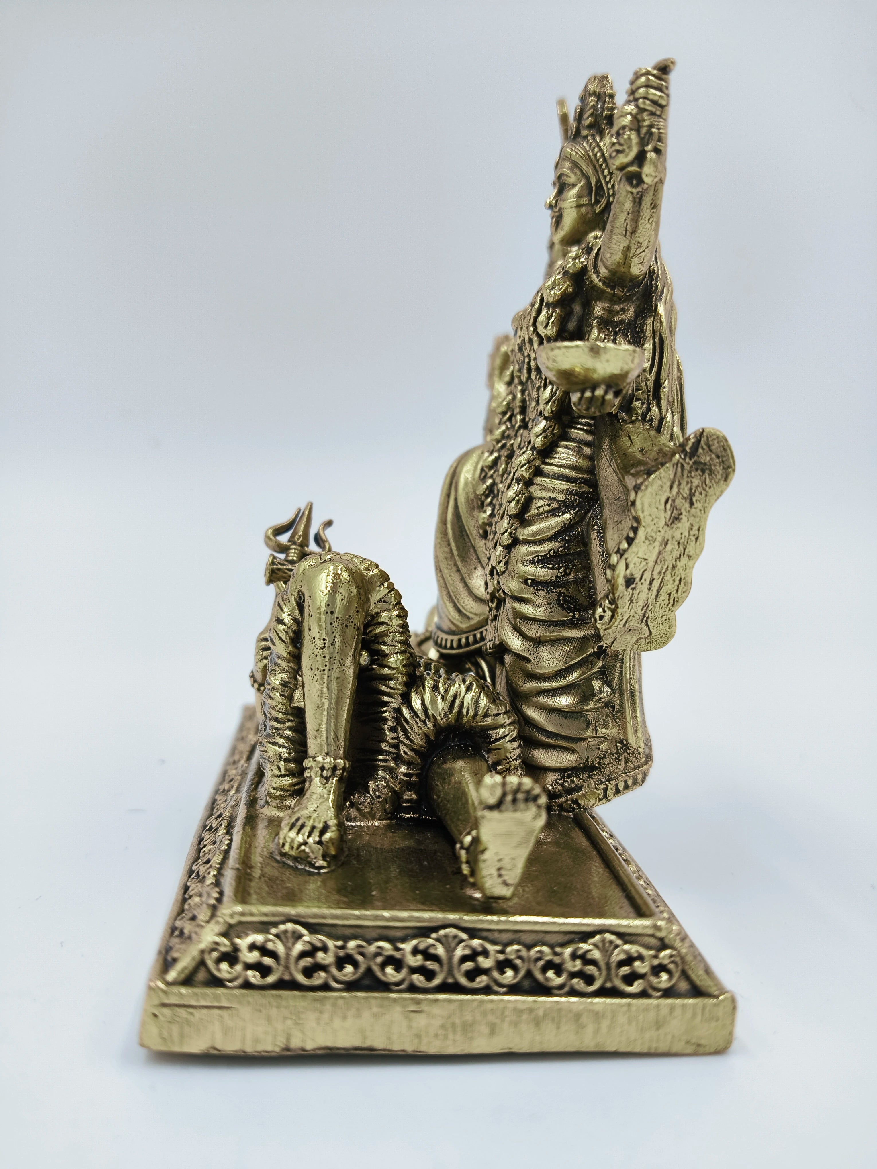 Side view of small brass statue of deity Kalika seated on decorated base