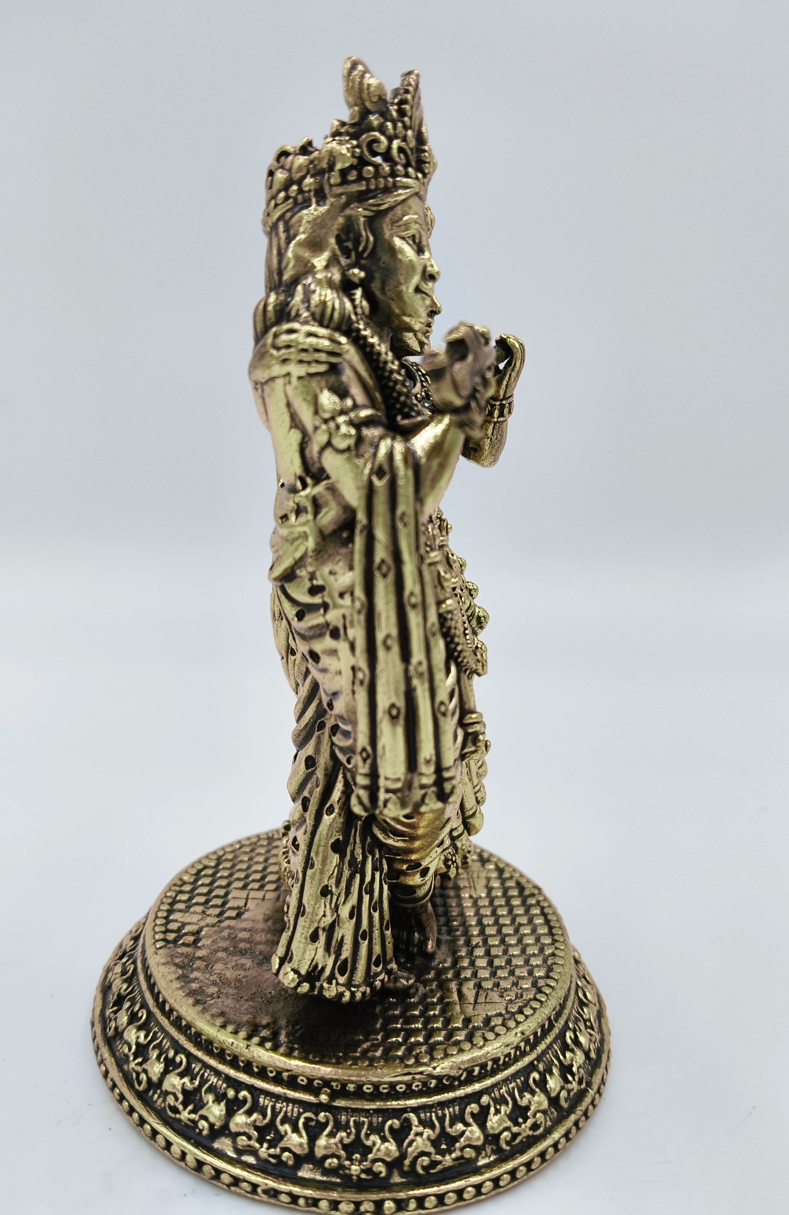 Side view of brass Radhakrishna statue on ornate round base