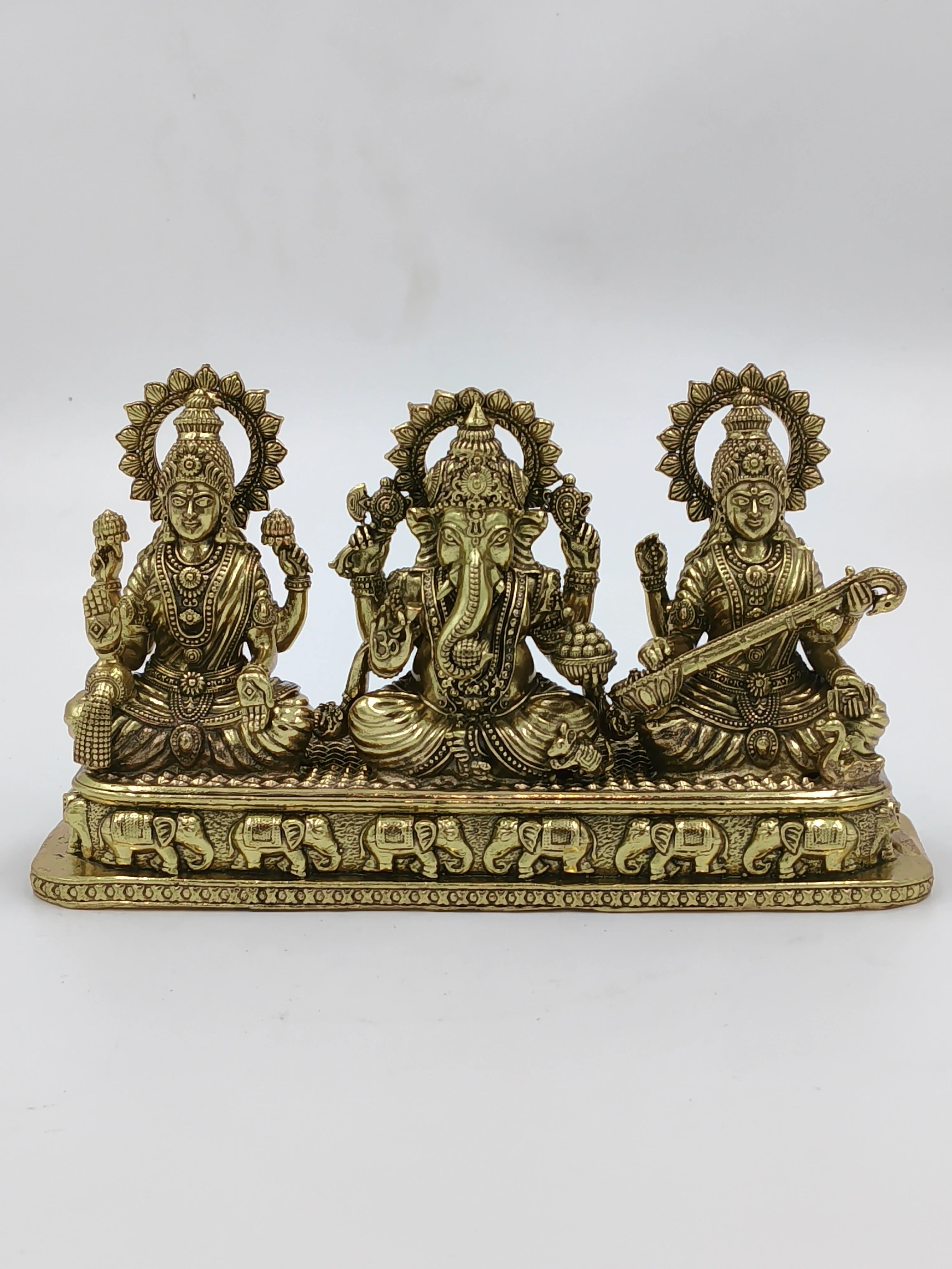 small brass sculpture of Lakshmi, Ganesh, and Saraswathi on a decorative base