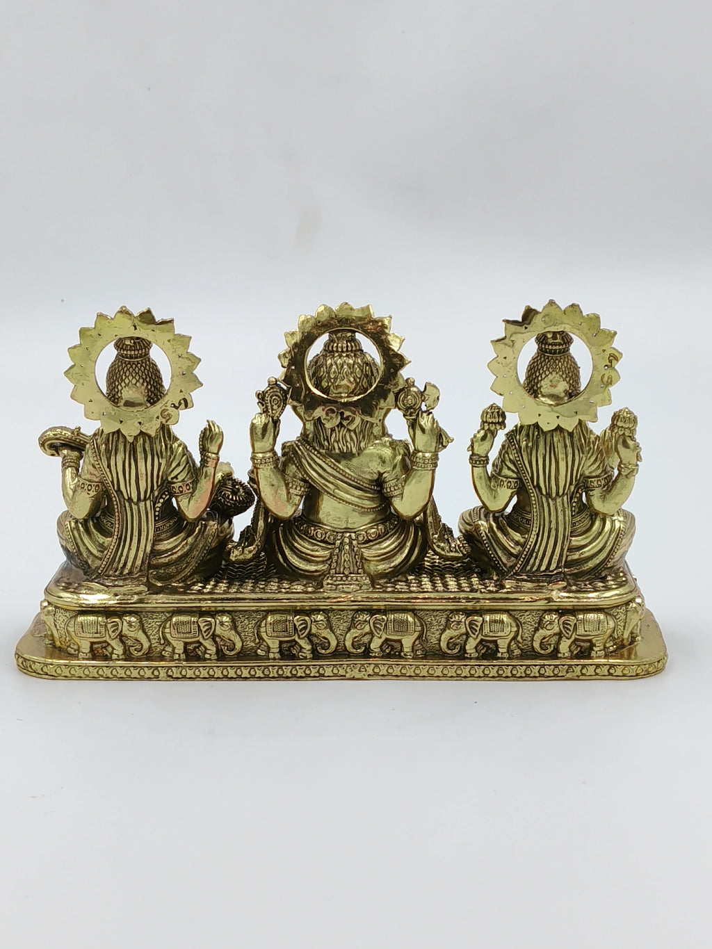 Back view of small brass sculpture featuring Lakshmi, Ganesh, and Saraswathi on rectangular base