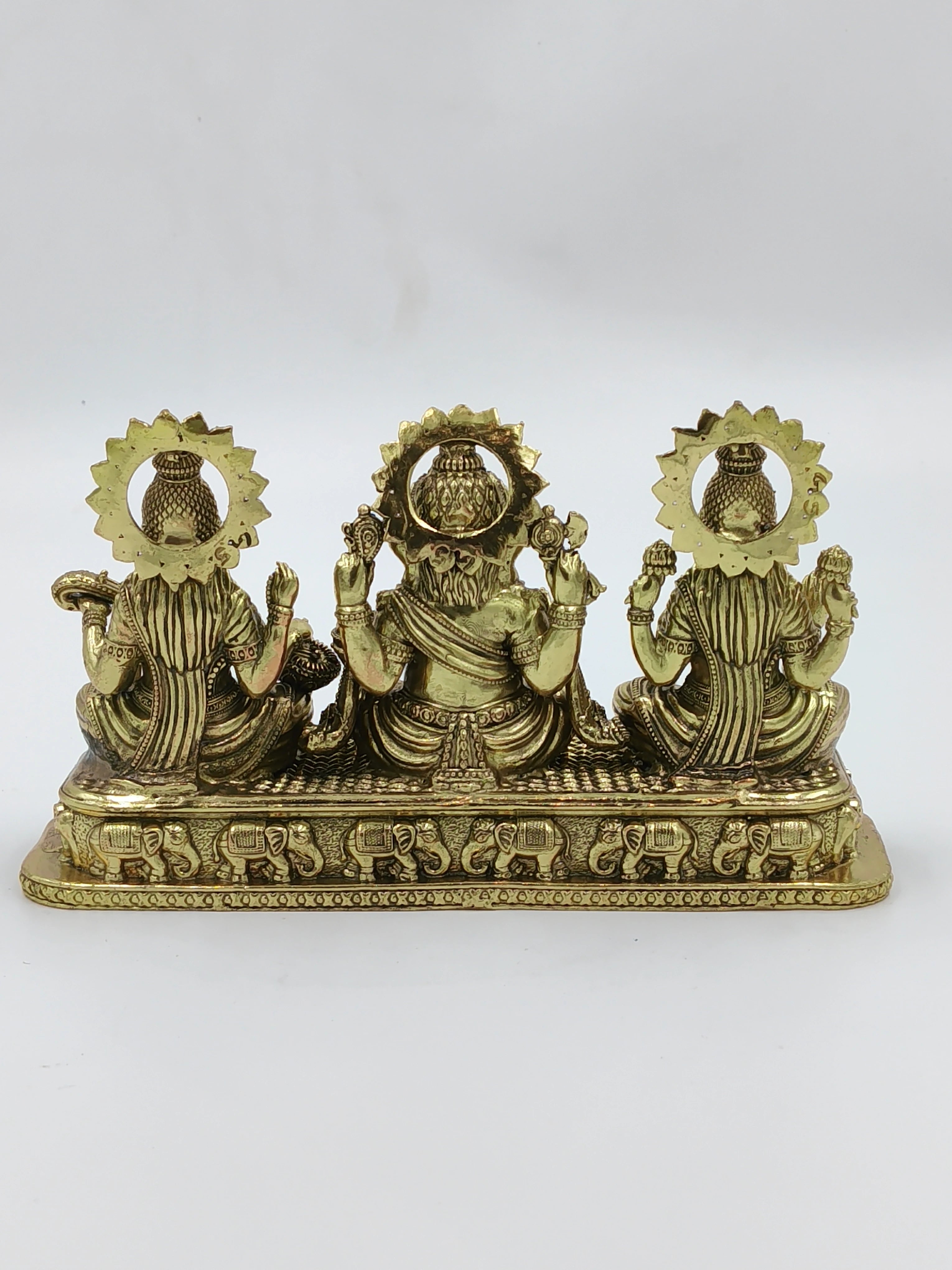 Back view of small brass sculpture featuring Lakshmi, Ganesh, and Saraswathi on rectangular base