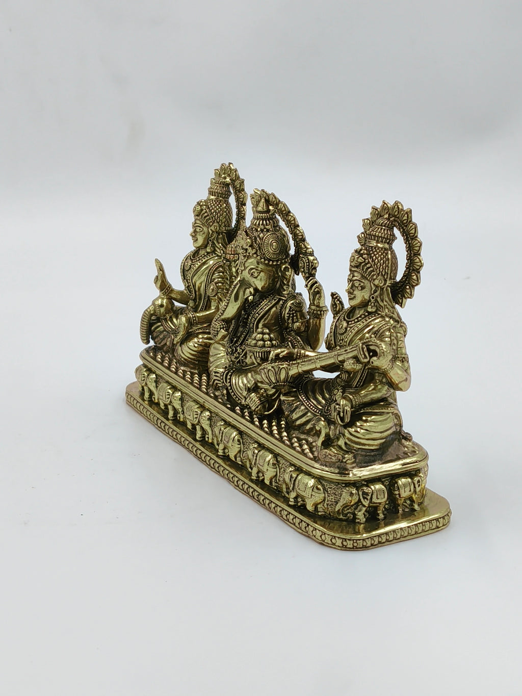 Small brass sculpture of Lakshmi, Ganesh, and Saraswathi seated on a decorated base