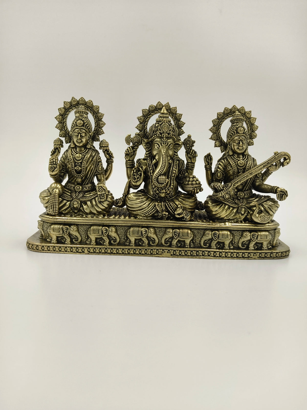 Brass tabletop sculpture of Lakshmi, Ganesh, and Saraswathi seated with decorative base