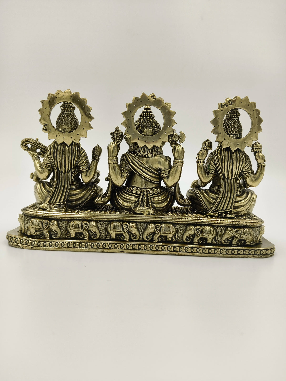 Back view of small brass sculpture featuring Lakshmi, Ganesh, and Saraswathi idols on a decorative base