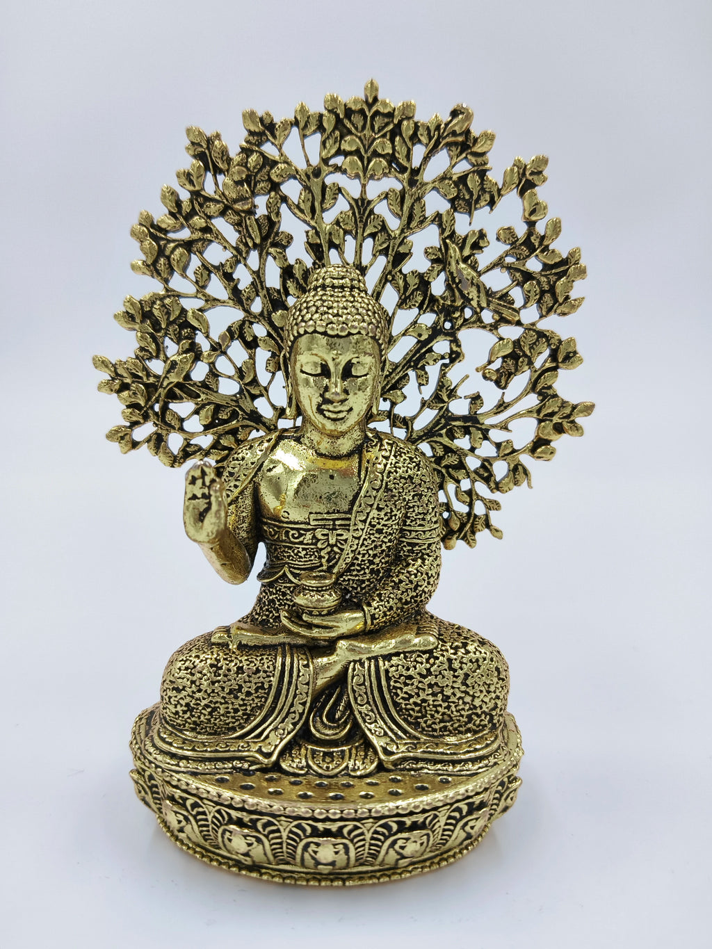 Small brass Buddha figurine seated in meditation with intricate tree design backdrop