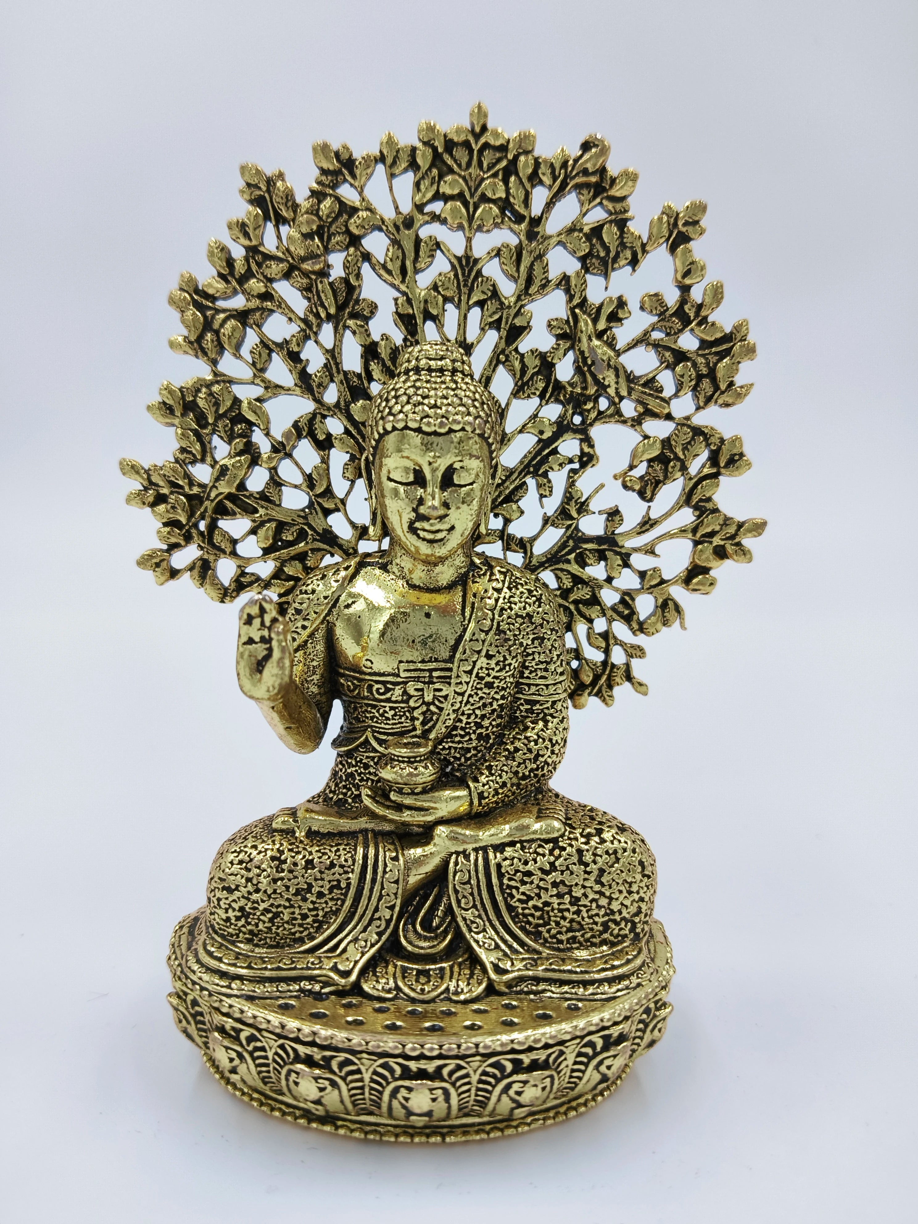 Small brass Buddha figurine seated in meditation with intricate tree design backdrop
