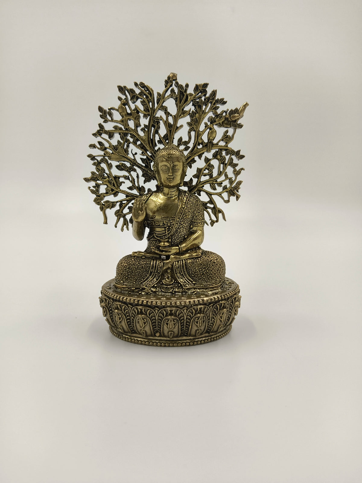 Small brass Buddha statue seated with detailed lotus pedestal and tree backdrop