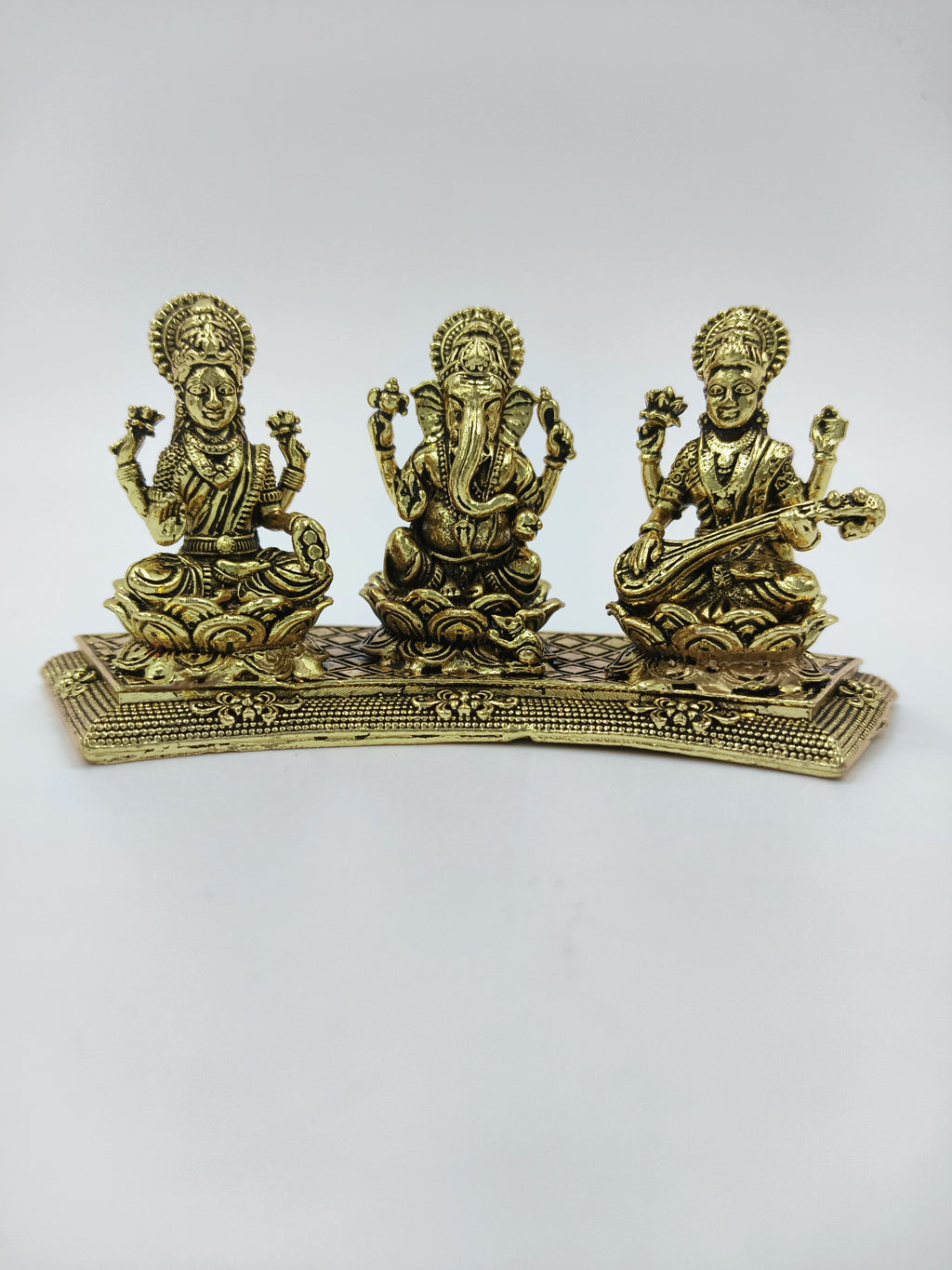 Mini brass statue featuring Lakshmi, Ganesh, and Saraswathi seated on a decorative base