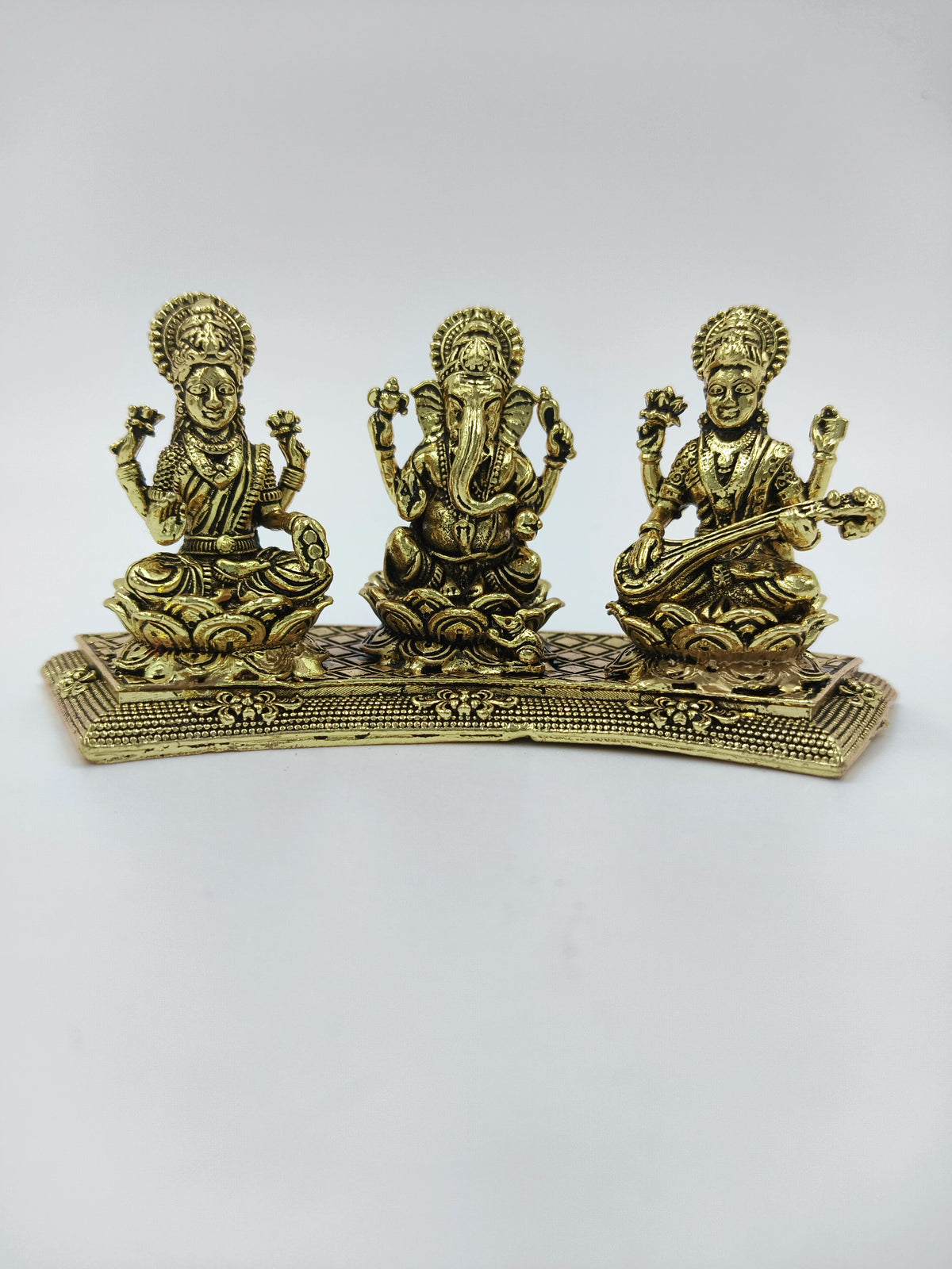 Mini brass statue featuring Lakshmi, Ganesh, and Saraswathi seated on a decorative base