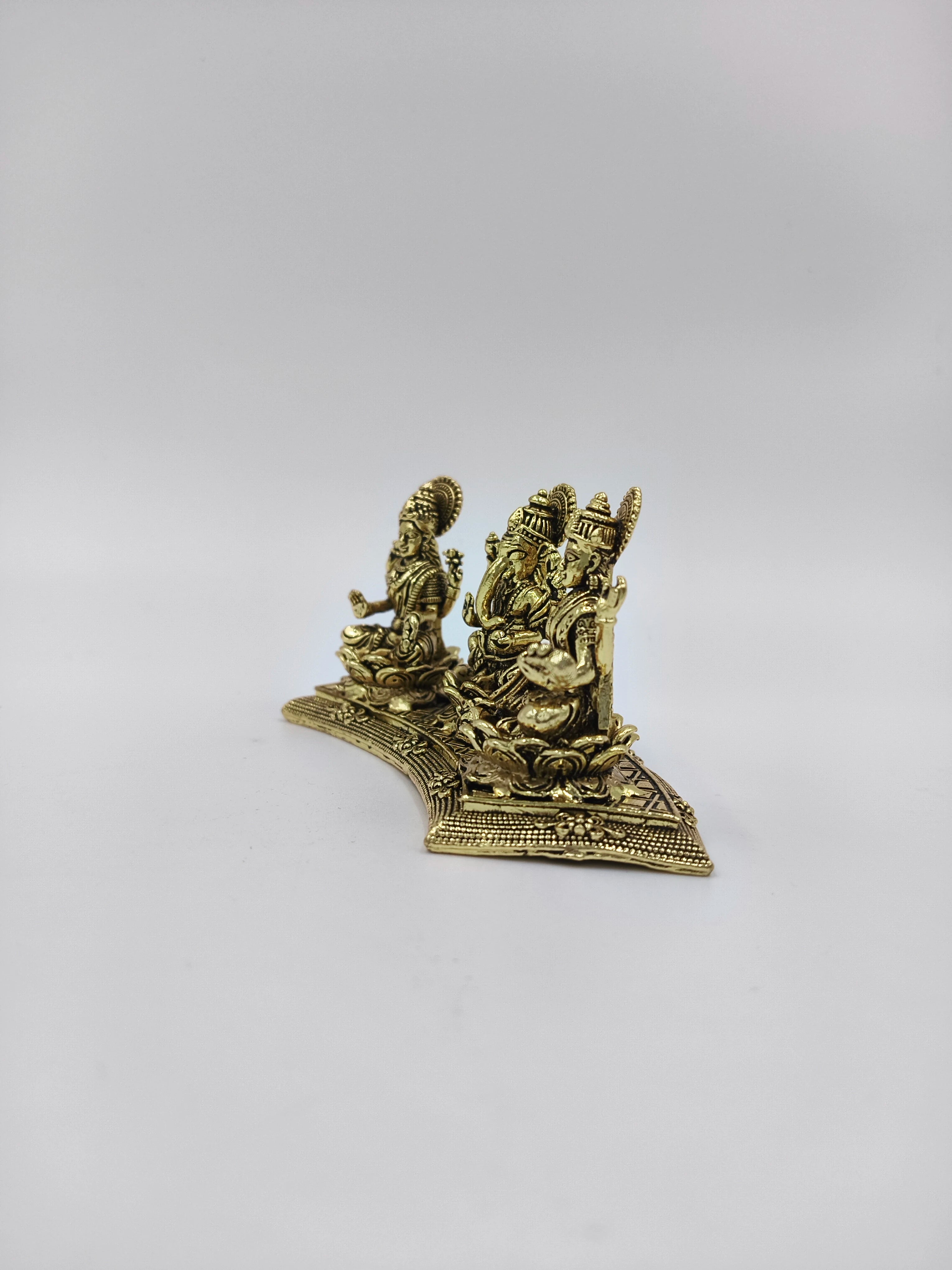 Mini brass statue depicting deities Lakshmi, Ganesh, and Saraswathi seated on ornate base