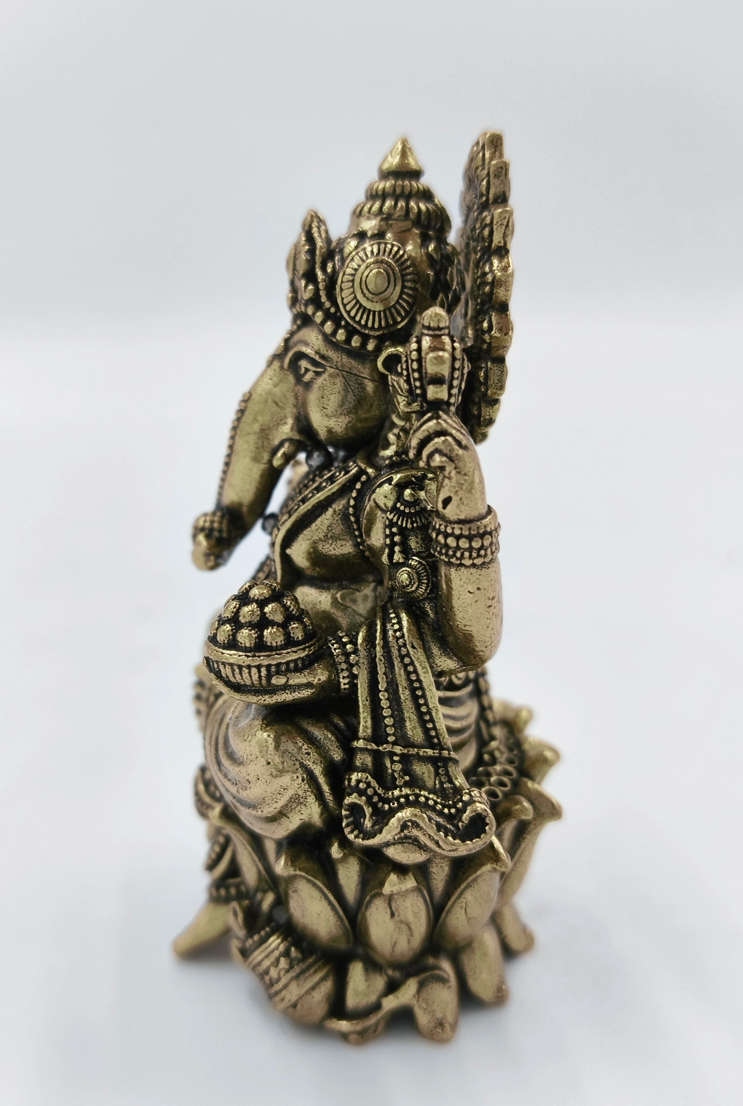 Mini brass statue of Ganesh seated on a lotus with intricate detailing
