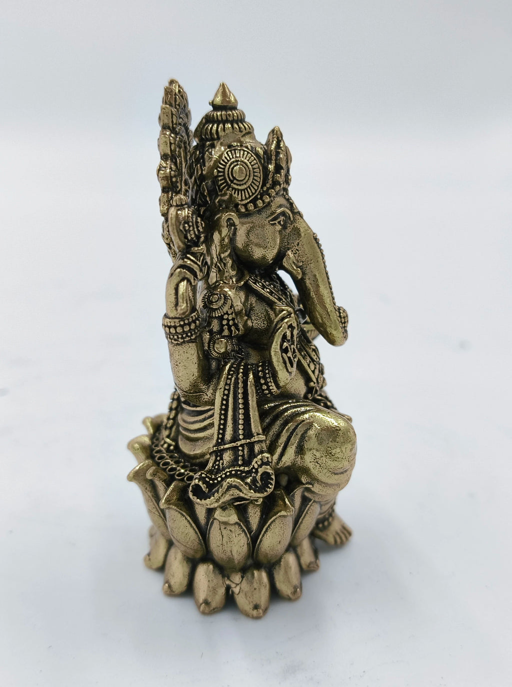 side view of a small brass Ganesh idol seated on a lotus pedestal