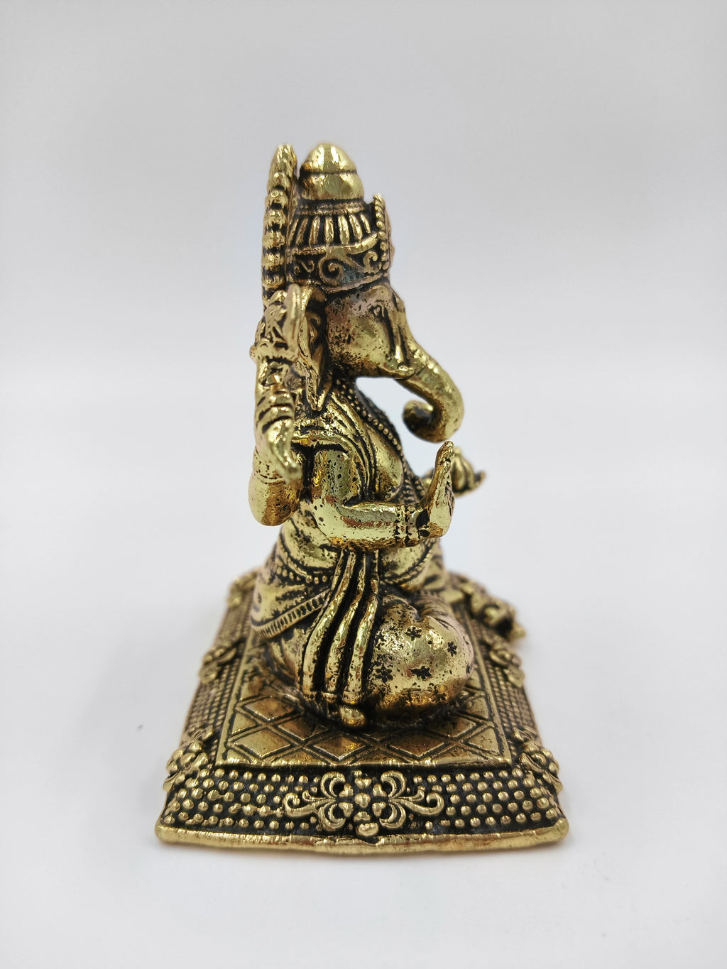 Small brass Ganesh statue sitting on an ornate platform, side view