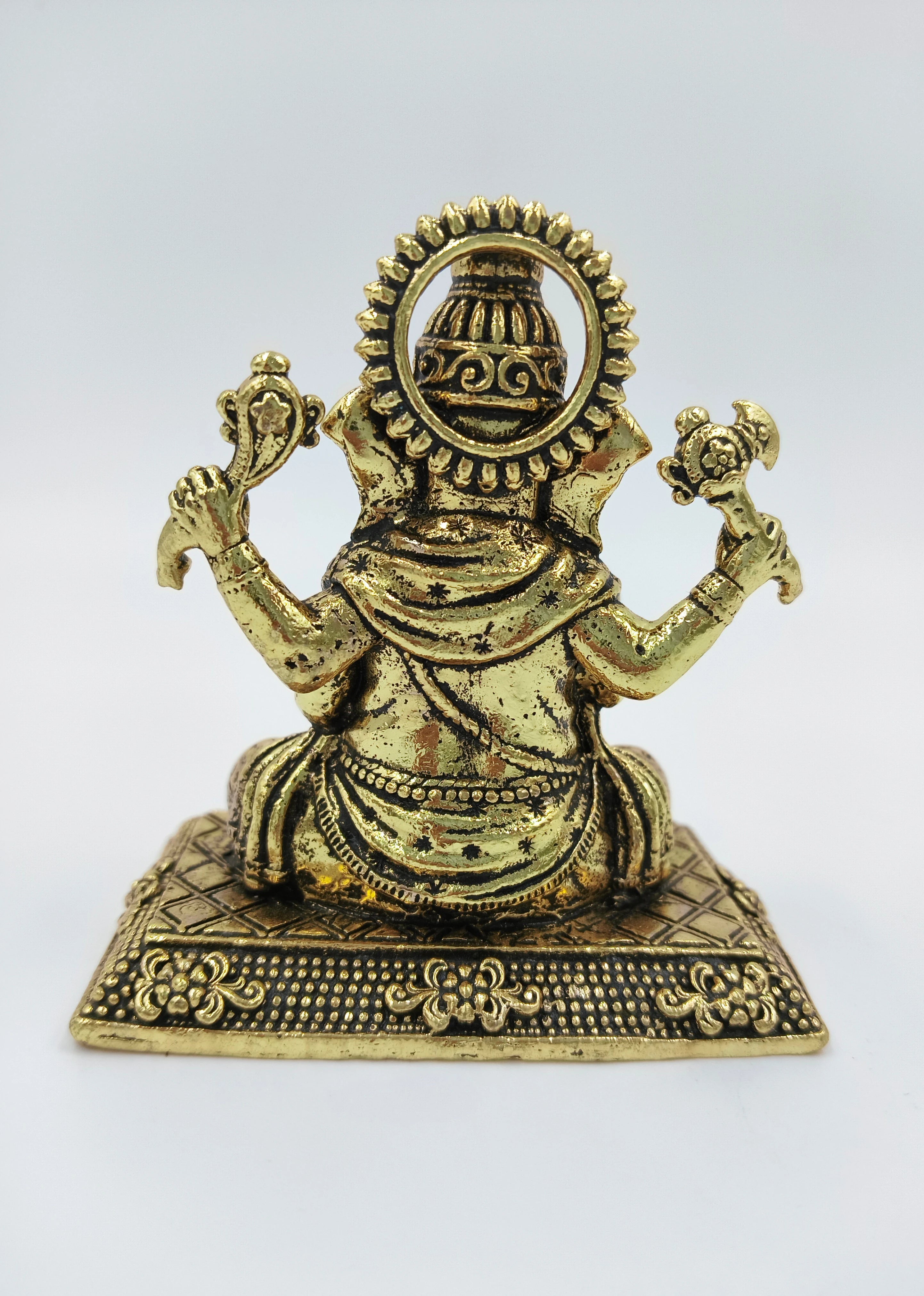 Back view of small brass Ganesh statue seated on decorated base