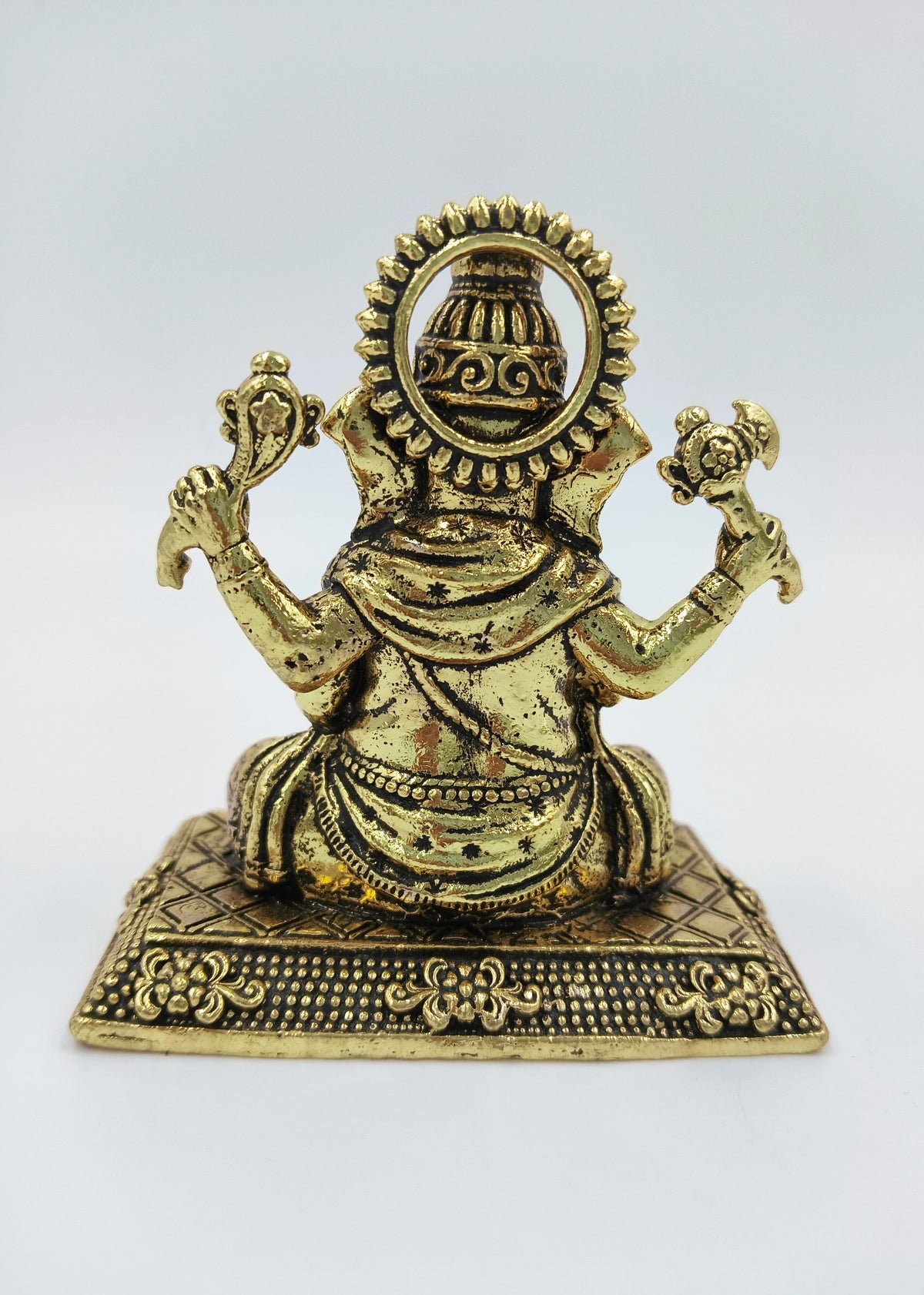 Back view of small brass Ganesh statue seated on decorated base