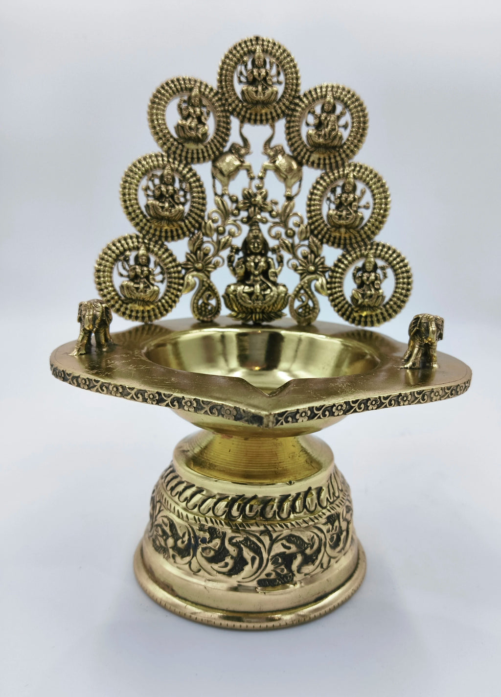 Brass Astalakshmi lamp with intricate floral engravings and deity figures on back panel