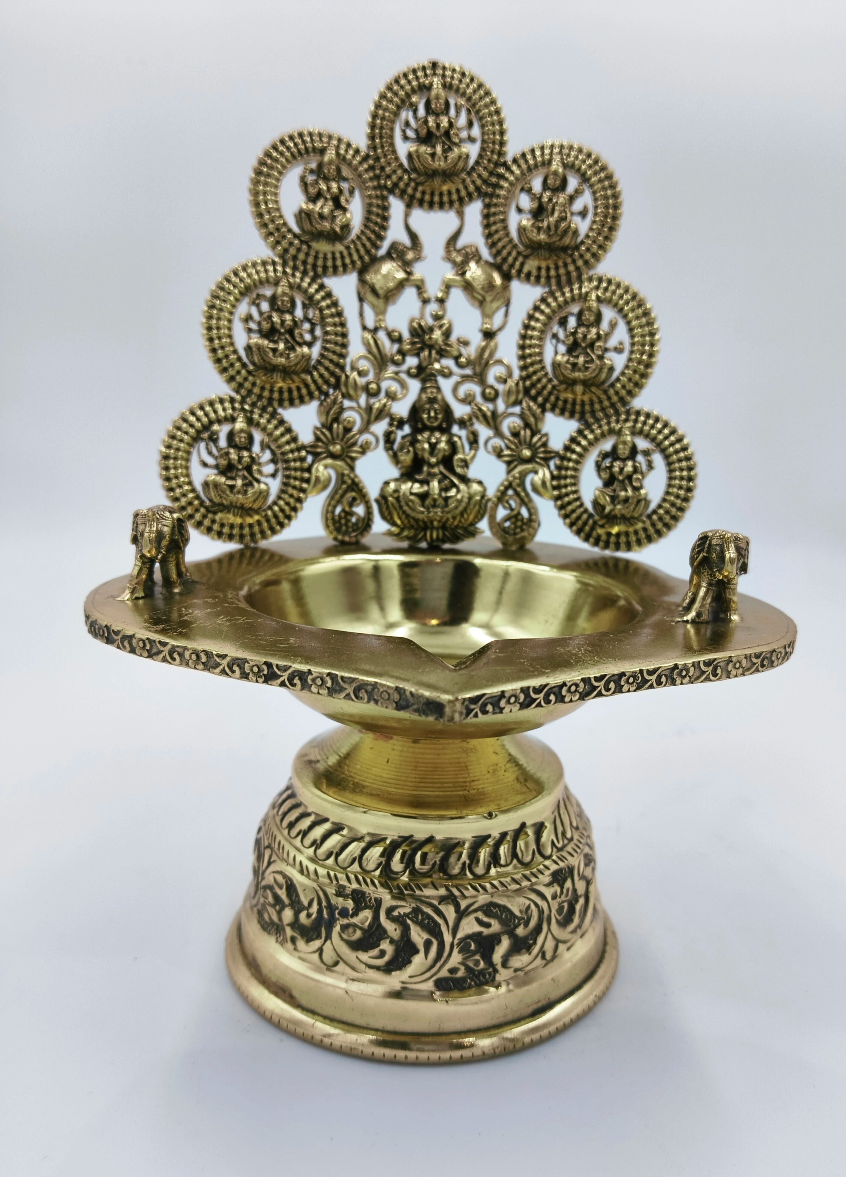 Brass Astalakshmi lamp with intricate floral engravings and deity figures on back panel