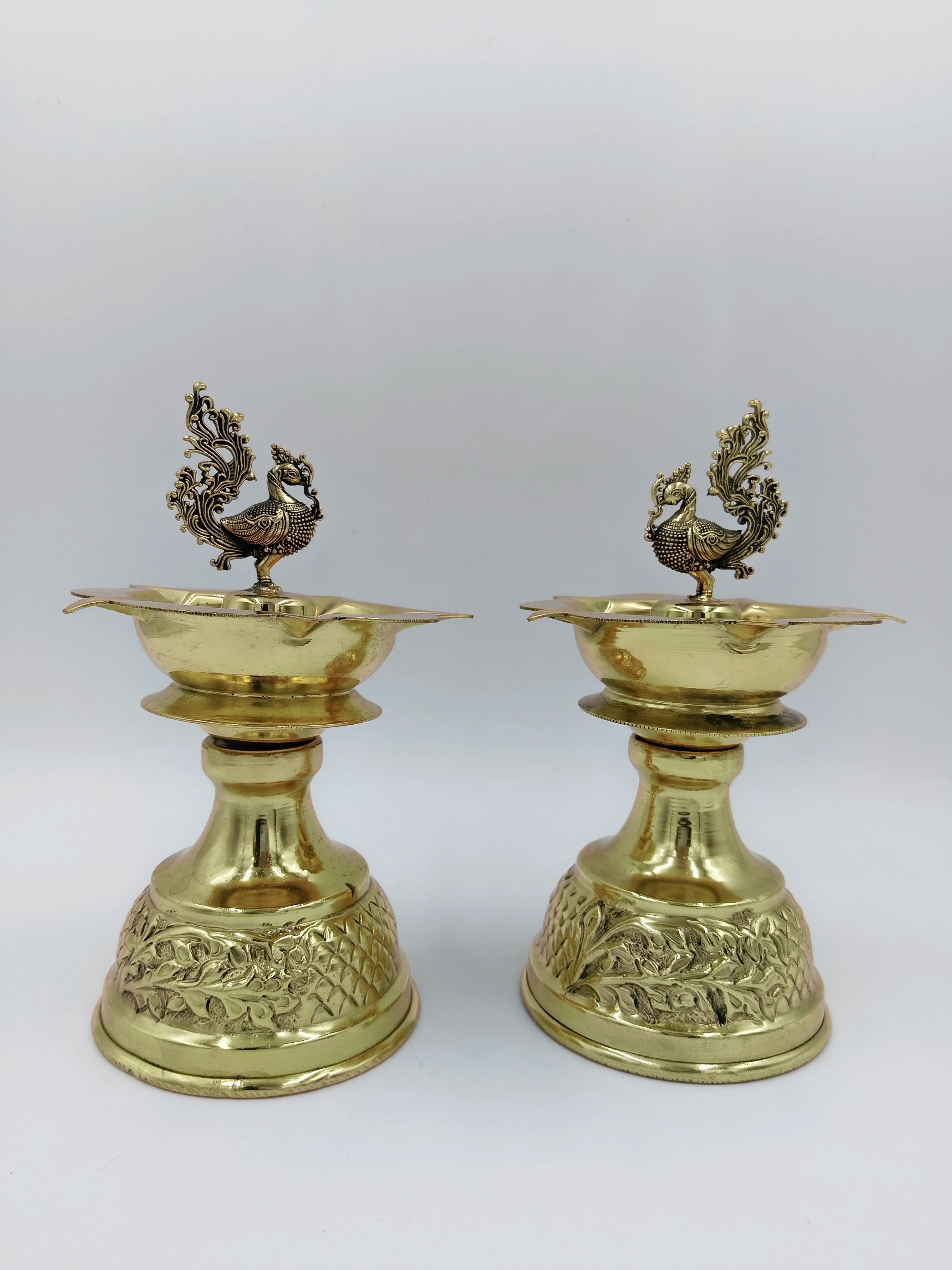 Pair of large brass diya oil lamps with decorative peacock motifs on top
