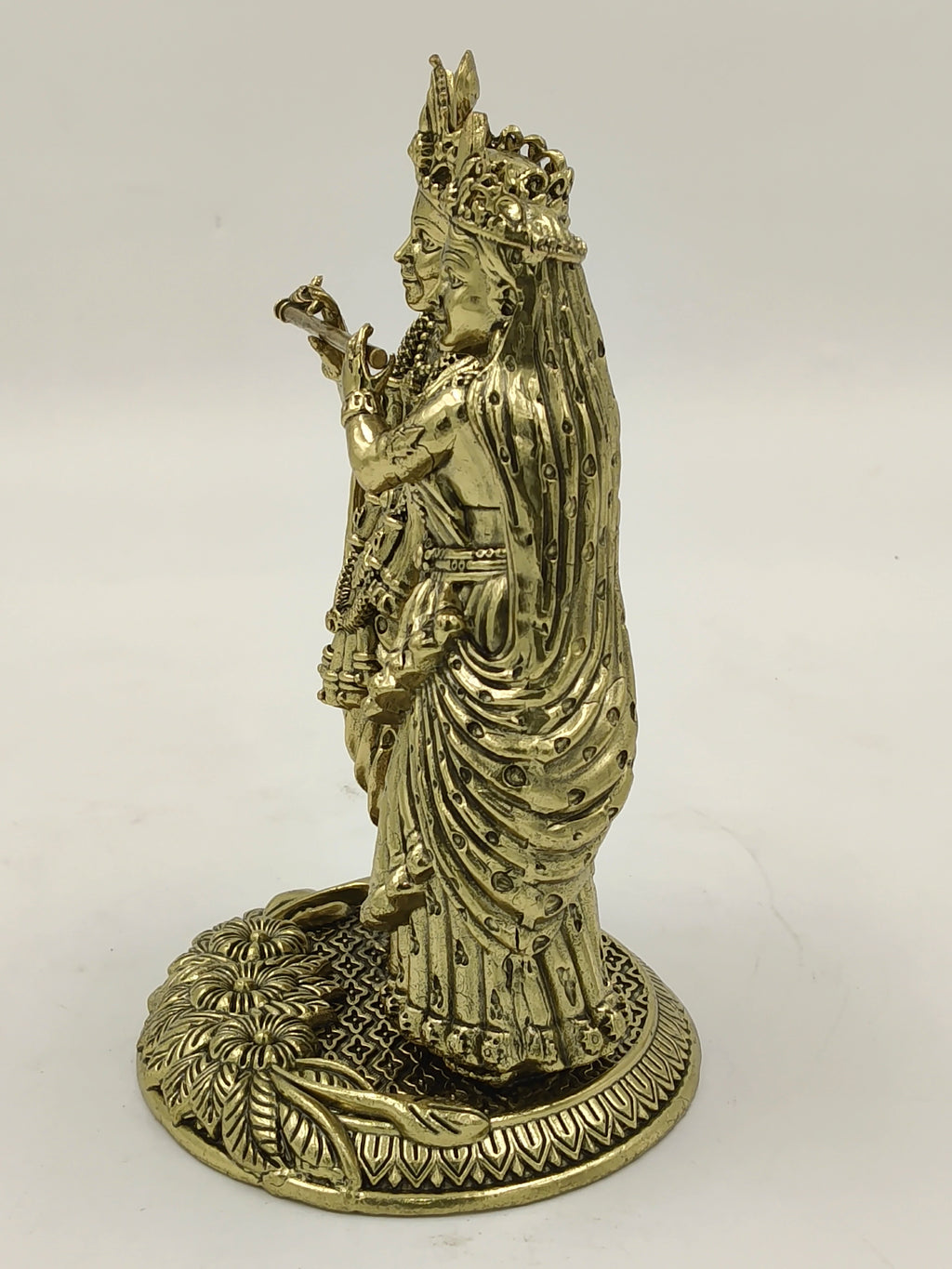 Side view of brass sculpture depicting Radhakrishna standing on decorated base