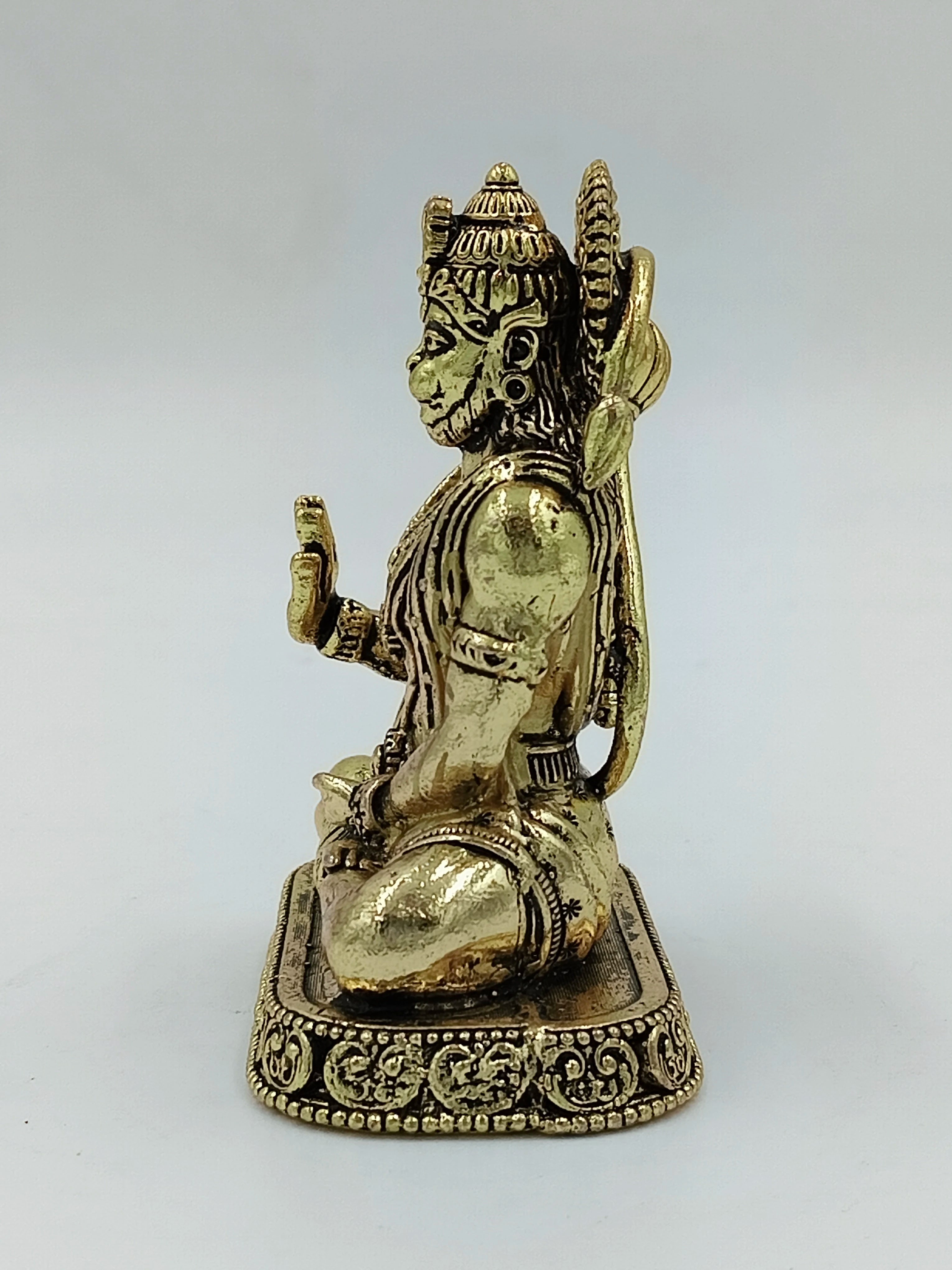 Small brass Hanuman statue seated with raised hand on decorative base, side view