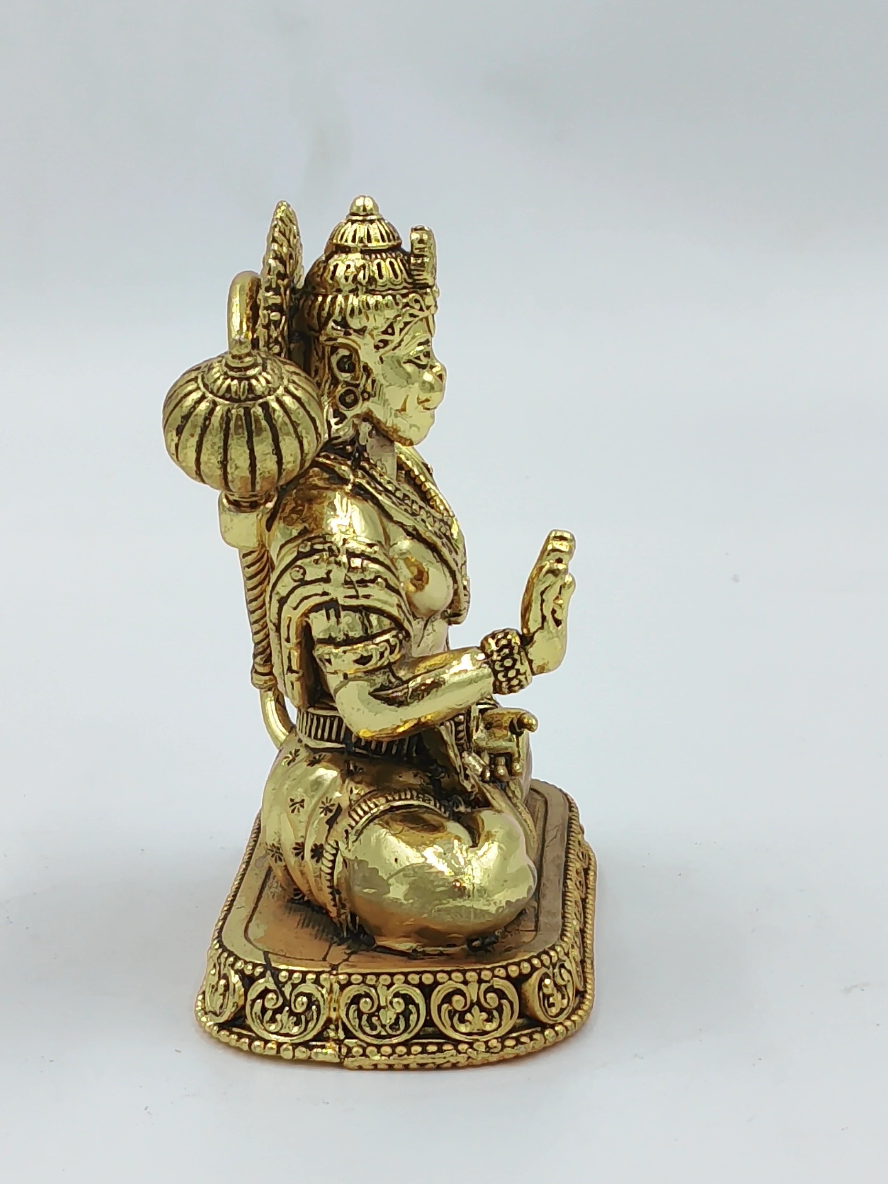 Side view of small brass Hanuman statue seated on an ornate base