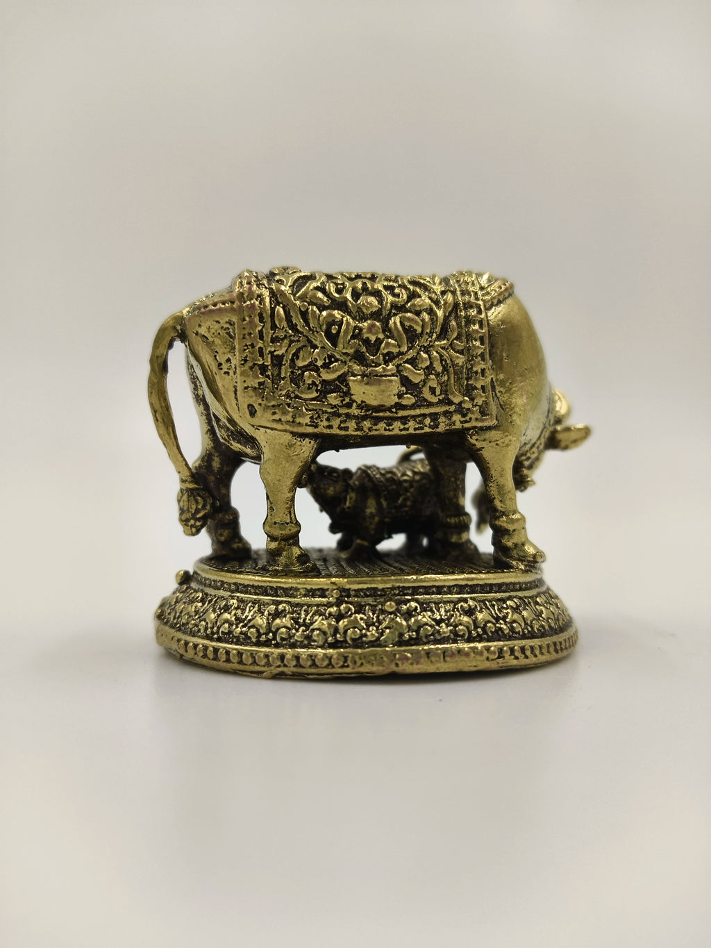 Mini brass sculpture of a cow with calf on decorated base, side view