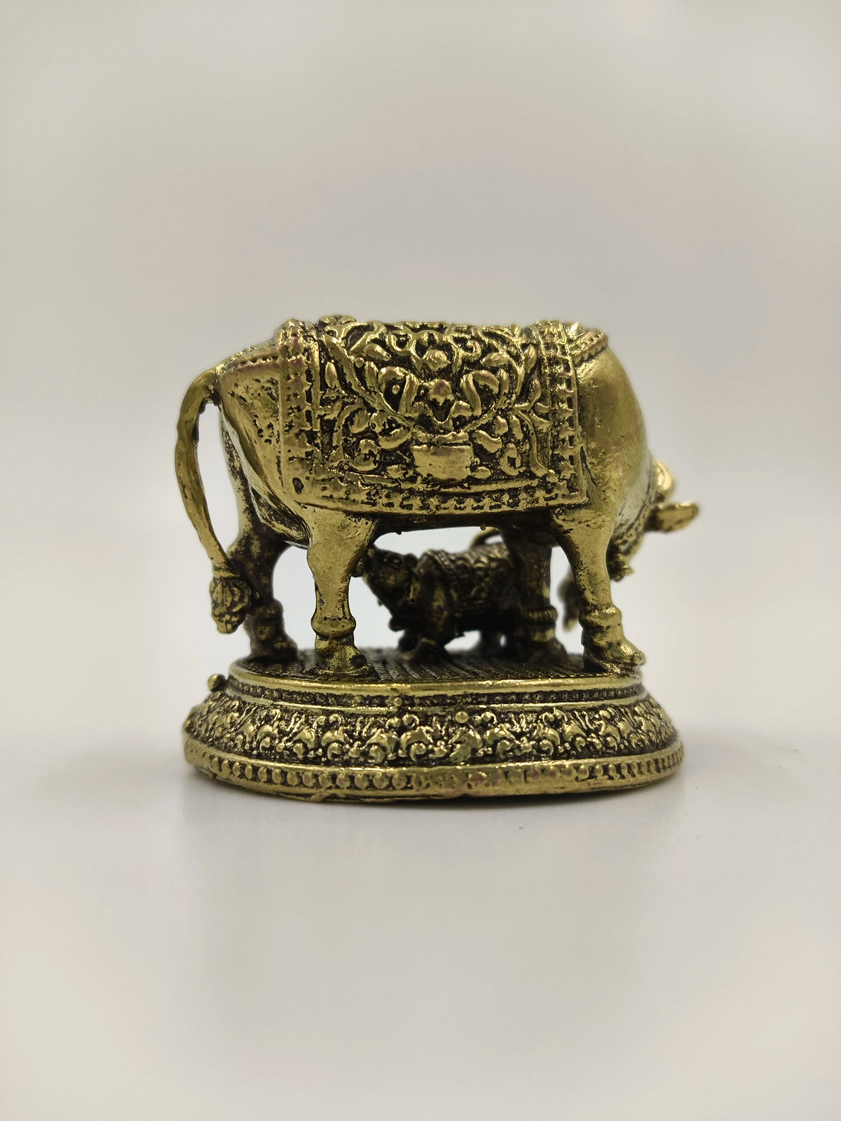 Mini brass sculpture of a cow with calf on decorated base, side view