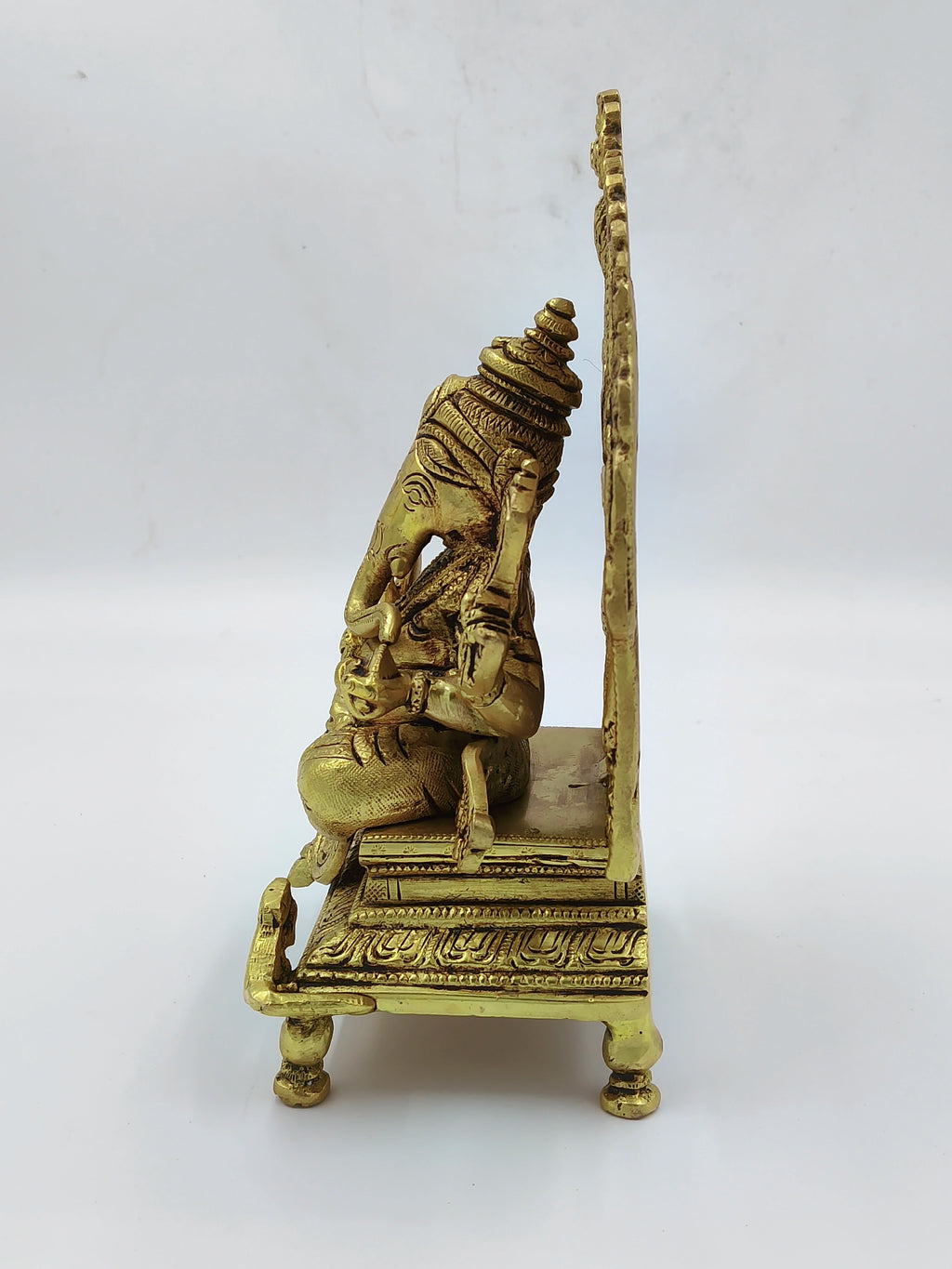 Side view of a large brass Ganesh statue sitting on a decorative throne