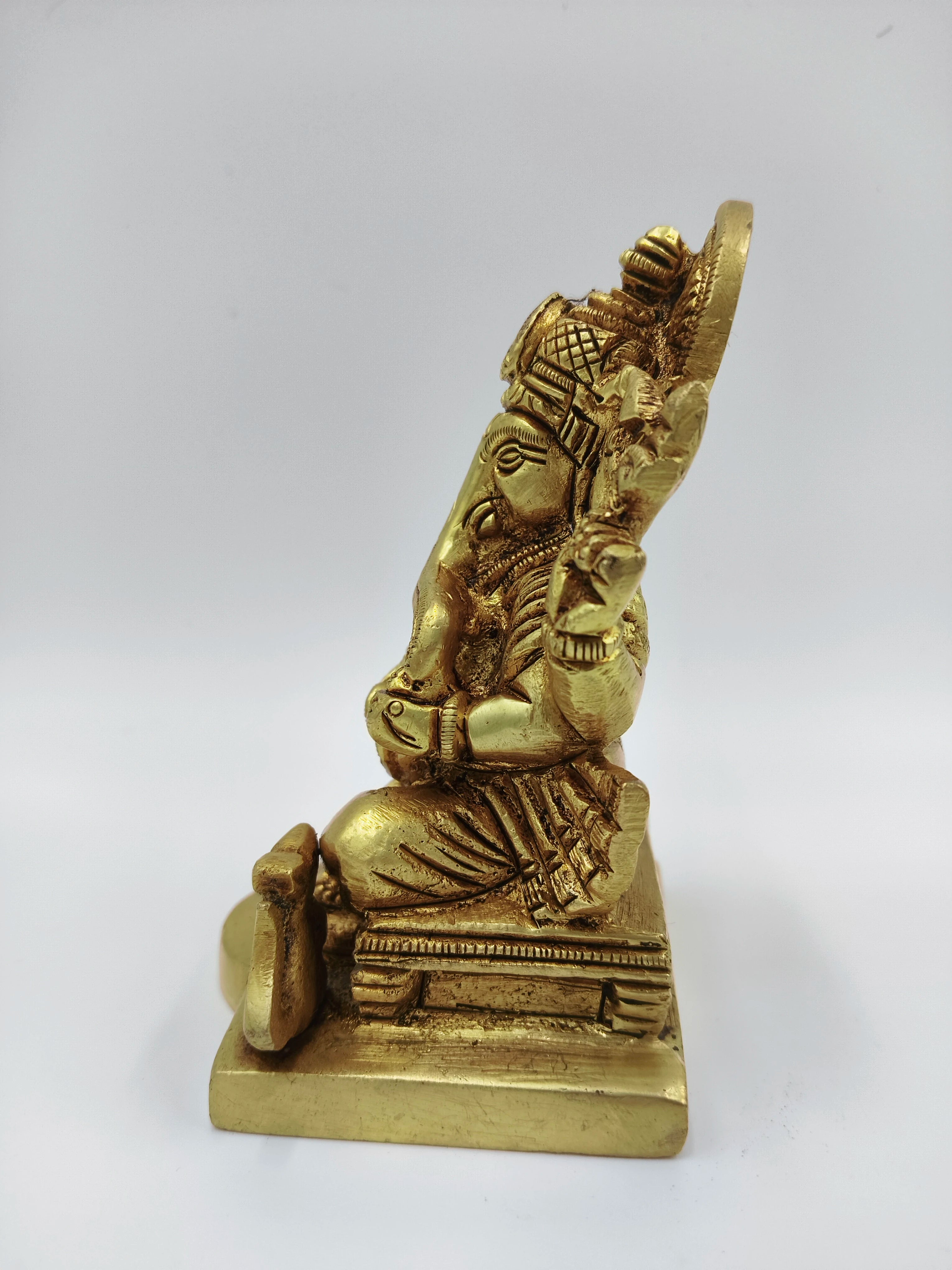 Side view of a small brass Ganesha sitting statue on a square base