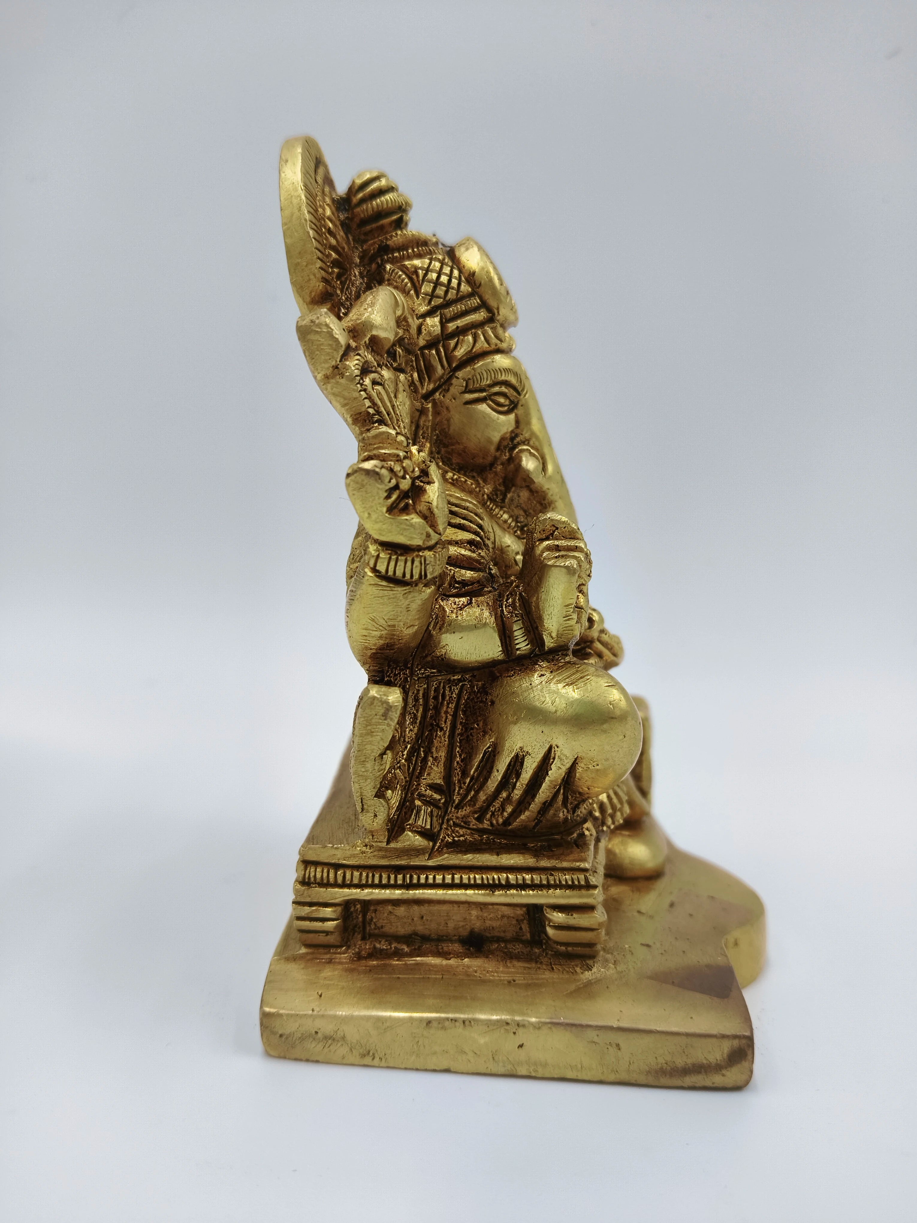 Side view of small brass statue of Lord Ganesha sitting on a platform