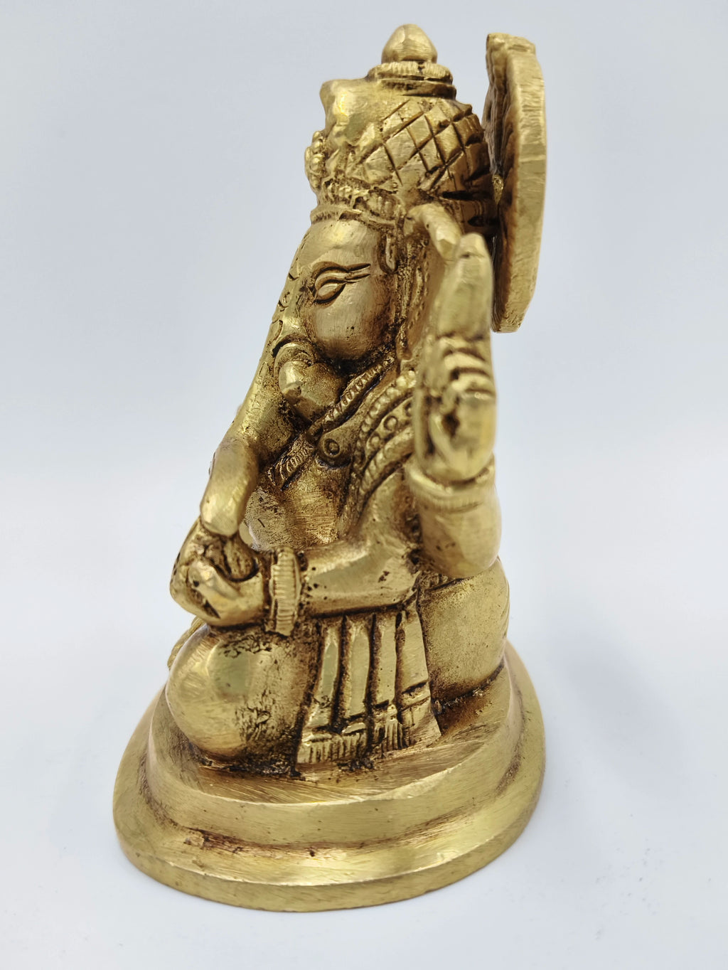 Side view of small brass Ganesha statue seated on round base