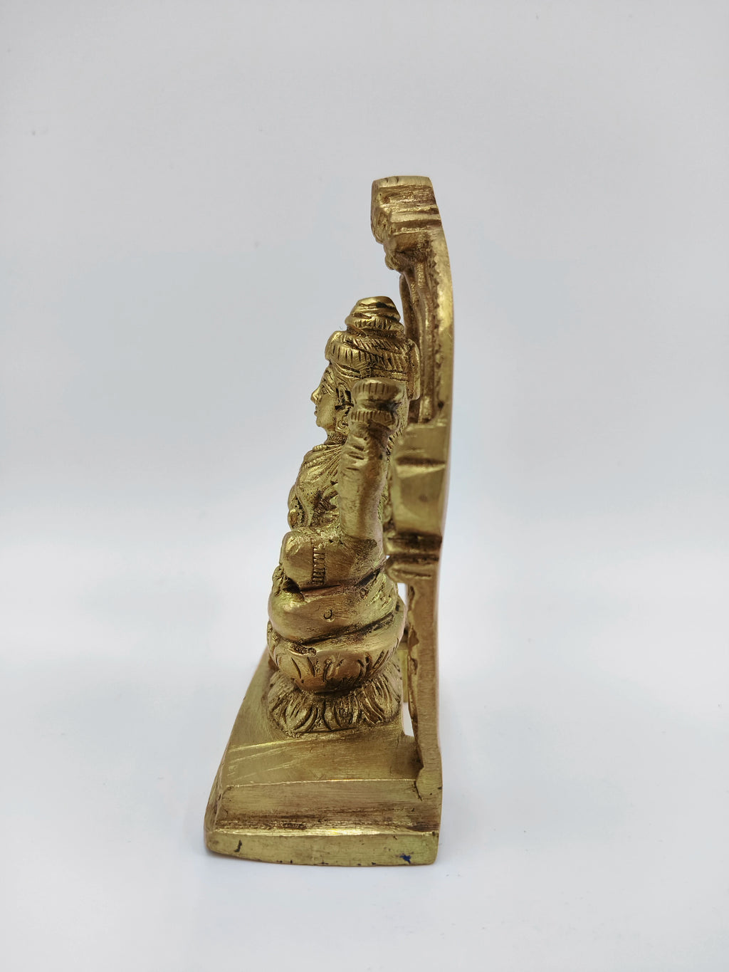 Side view of small brass Lakshmi statue seated on lotus with decorative arch