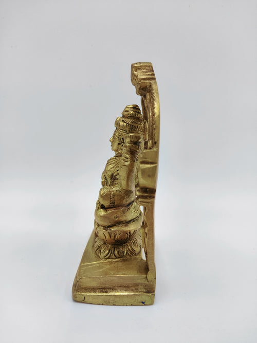 Side view of small brass Lakshmi statue seated on lotus with decorative arch