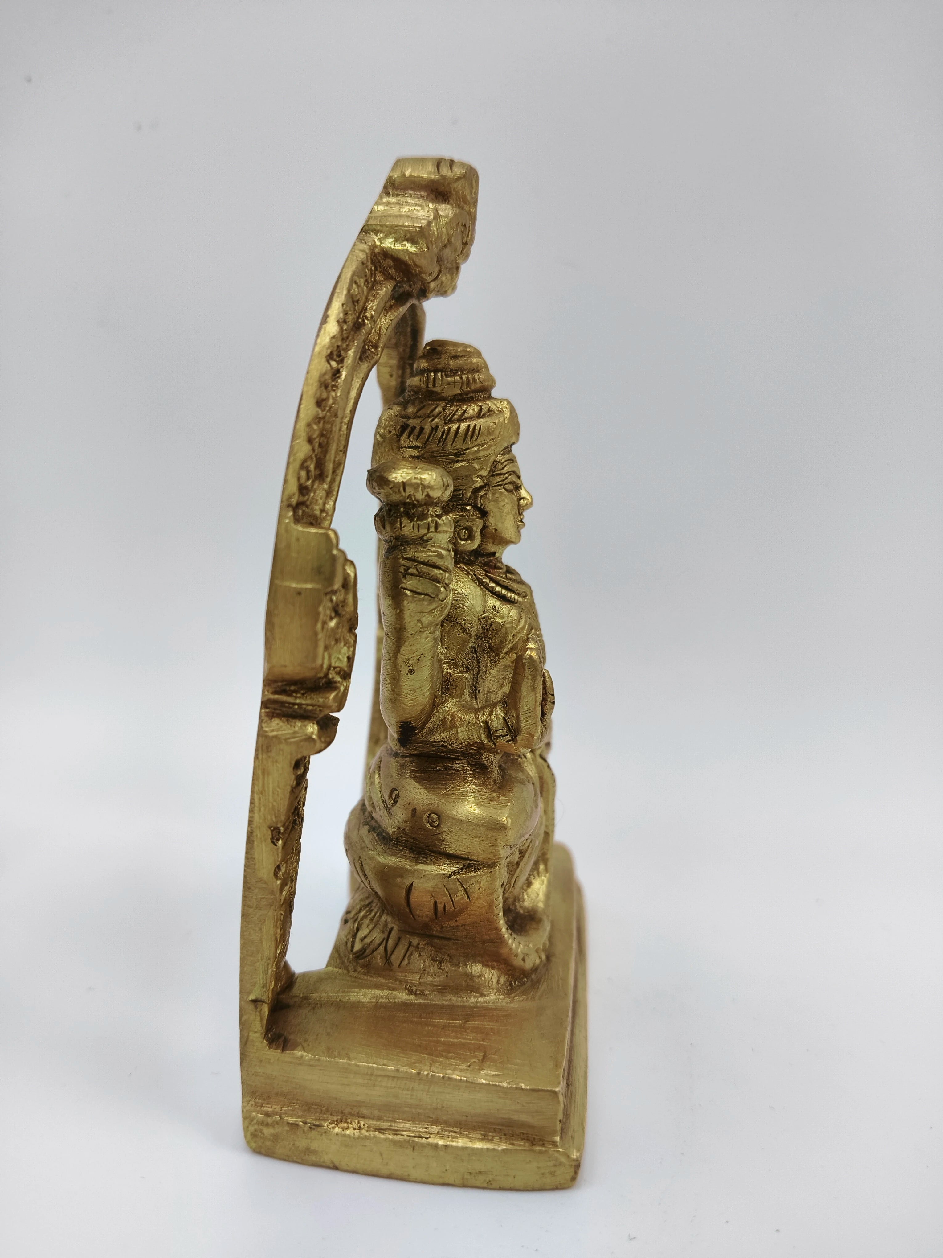 Side view of small brass Lakshmi statue seated on lotus with arch