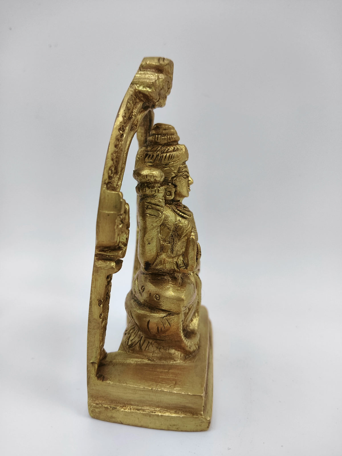 Side view of small brass Lakshmi statue seated on lotus with arch