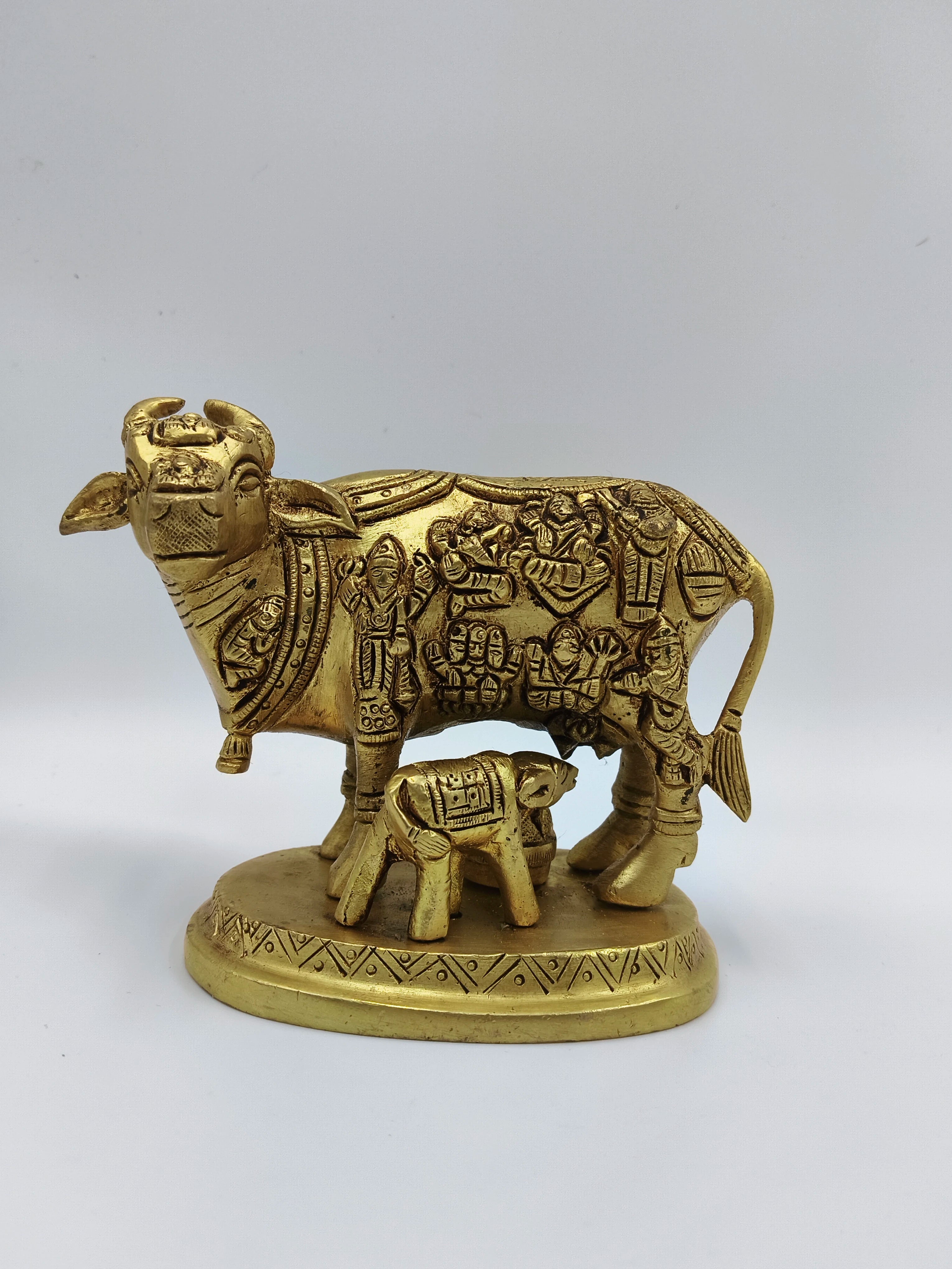 Small brass sculpture of cow and calf with intricate divine figure engravings