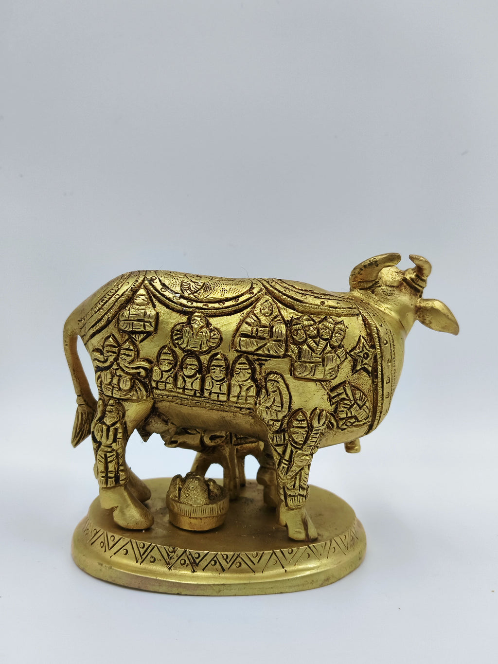 Brass sculpture of cow and calf with engraved divine figures on a round base
